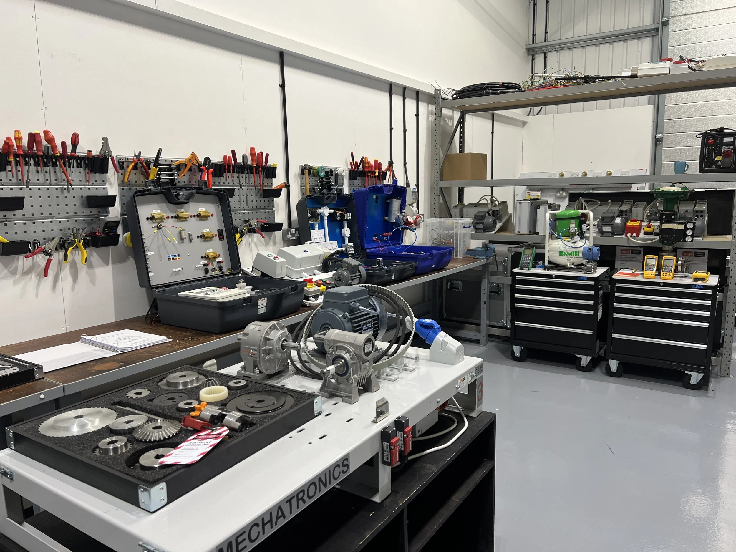 Workshop with tools, electronic components, and mechanical parts, including gears, motors, and testing equipment.
