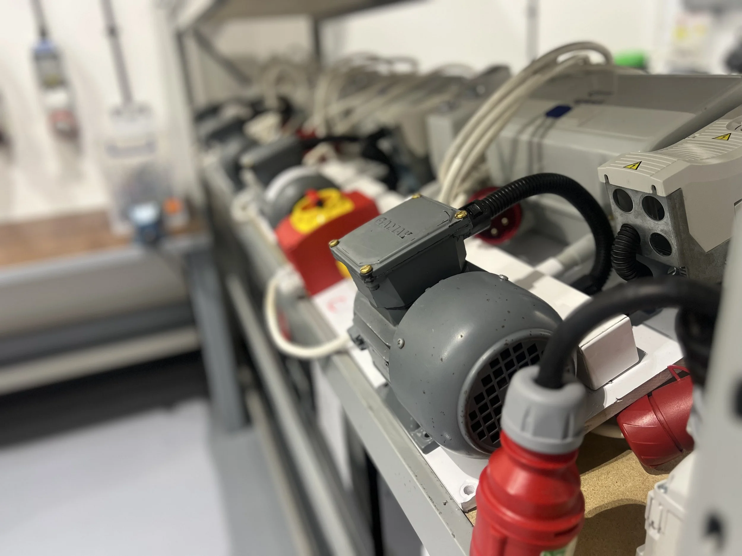 Close-up of electrical and mechanical components, including a motor, wiring, and circuit breakers, on a white workspace surface.