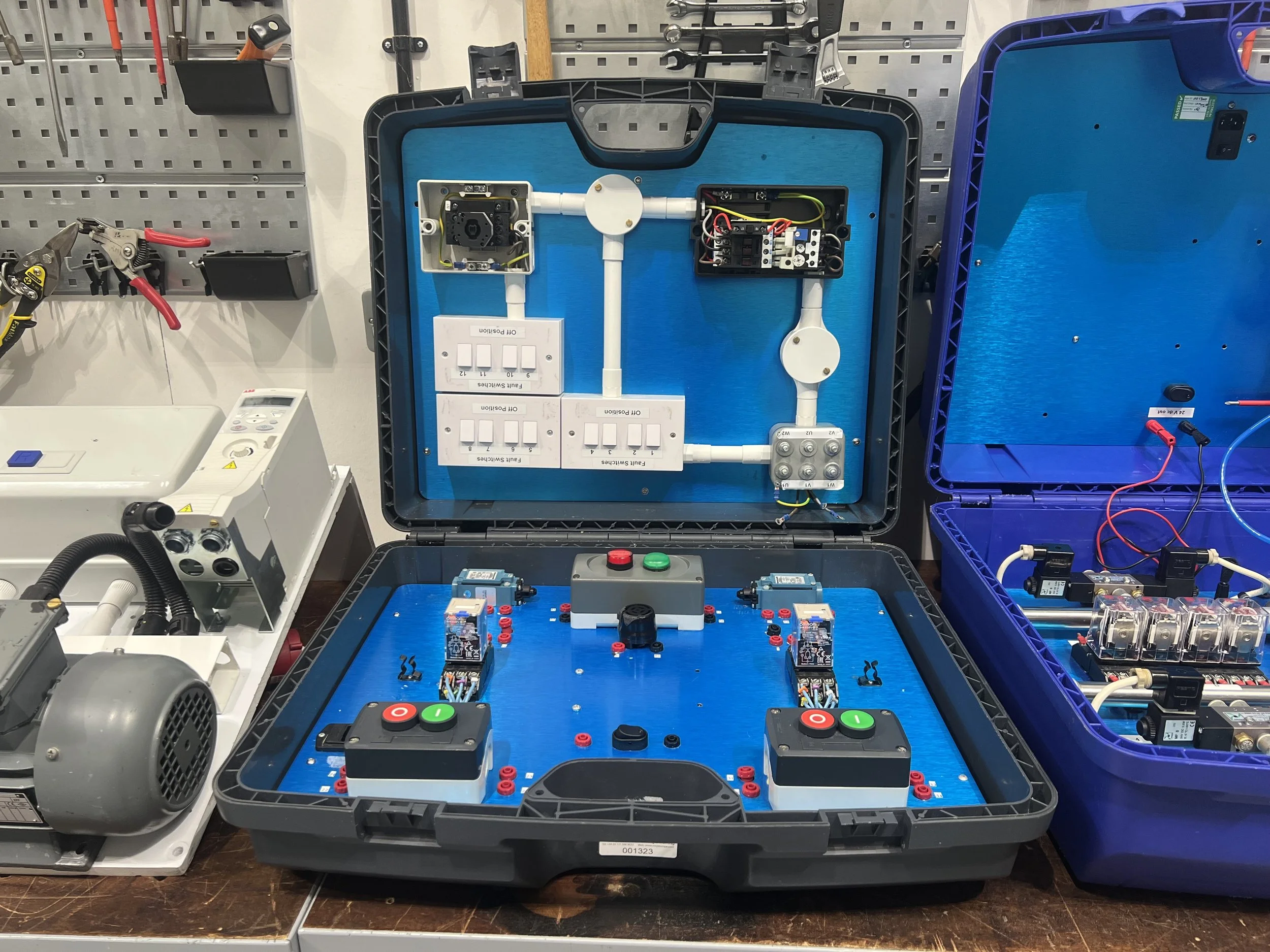 Open black and blue service cases with electronic components, wiring, switches, and circuit boards on a workbench.