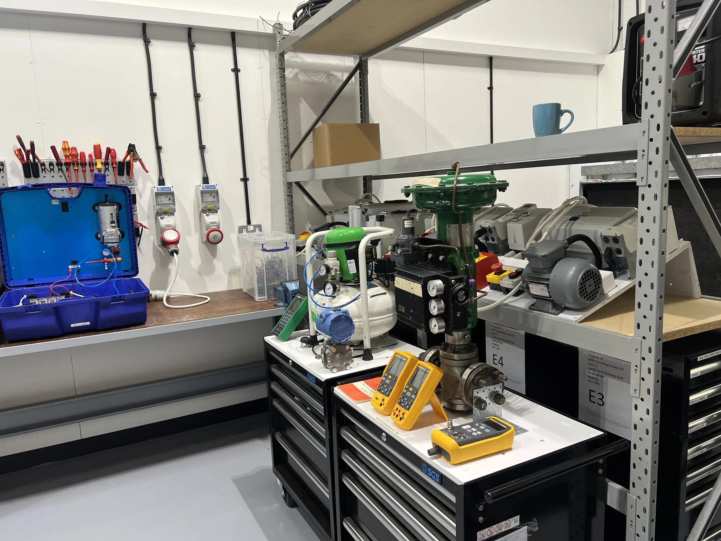 Workshop with tools, electronic equipment, and machinery, including meters, a green compressor, and a yellow multimeter on a black tool cart.