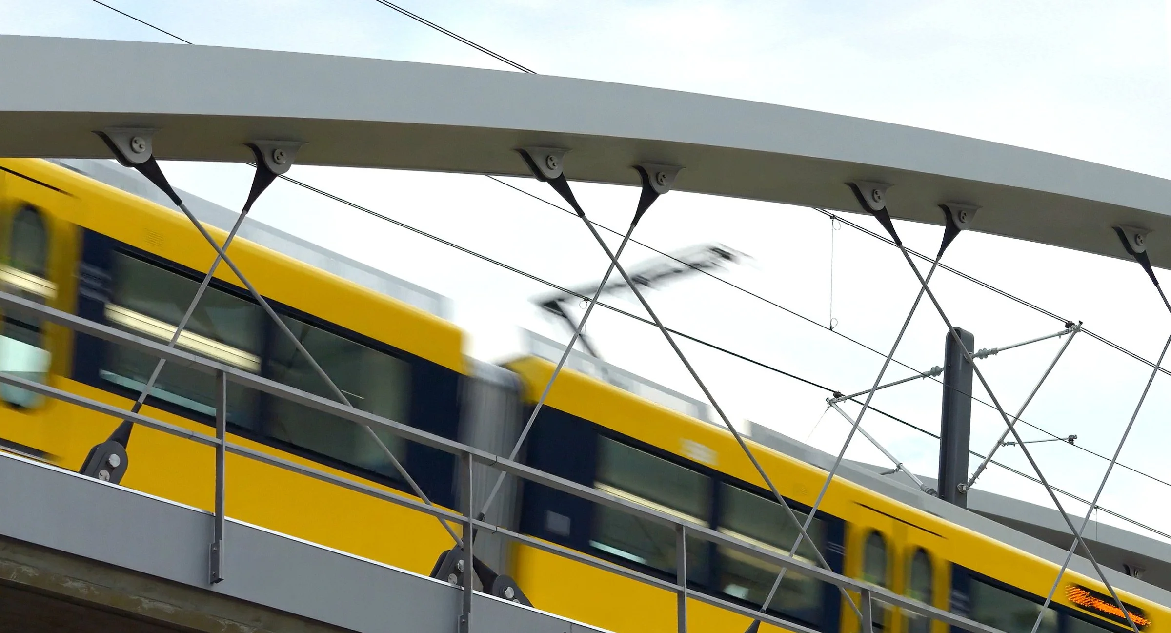 Schneller gelber Zug fährt über eine Brücke mit drahtlosen Oberleitungen.