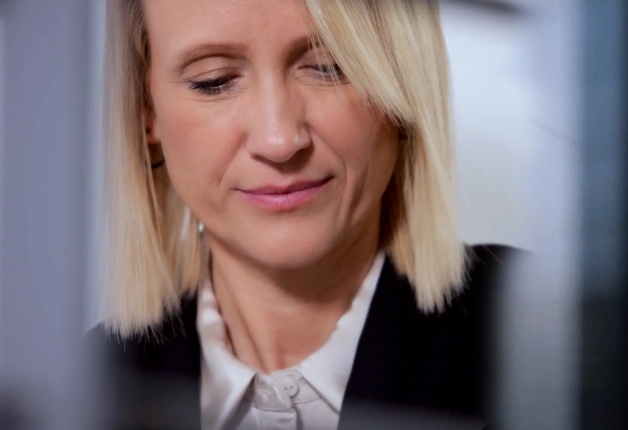 Nahaufnahme eines lachenden, blondhaarigen Frauen im Büro, die auf einen Bildschirm schaut.