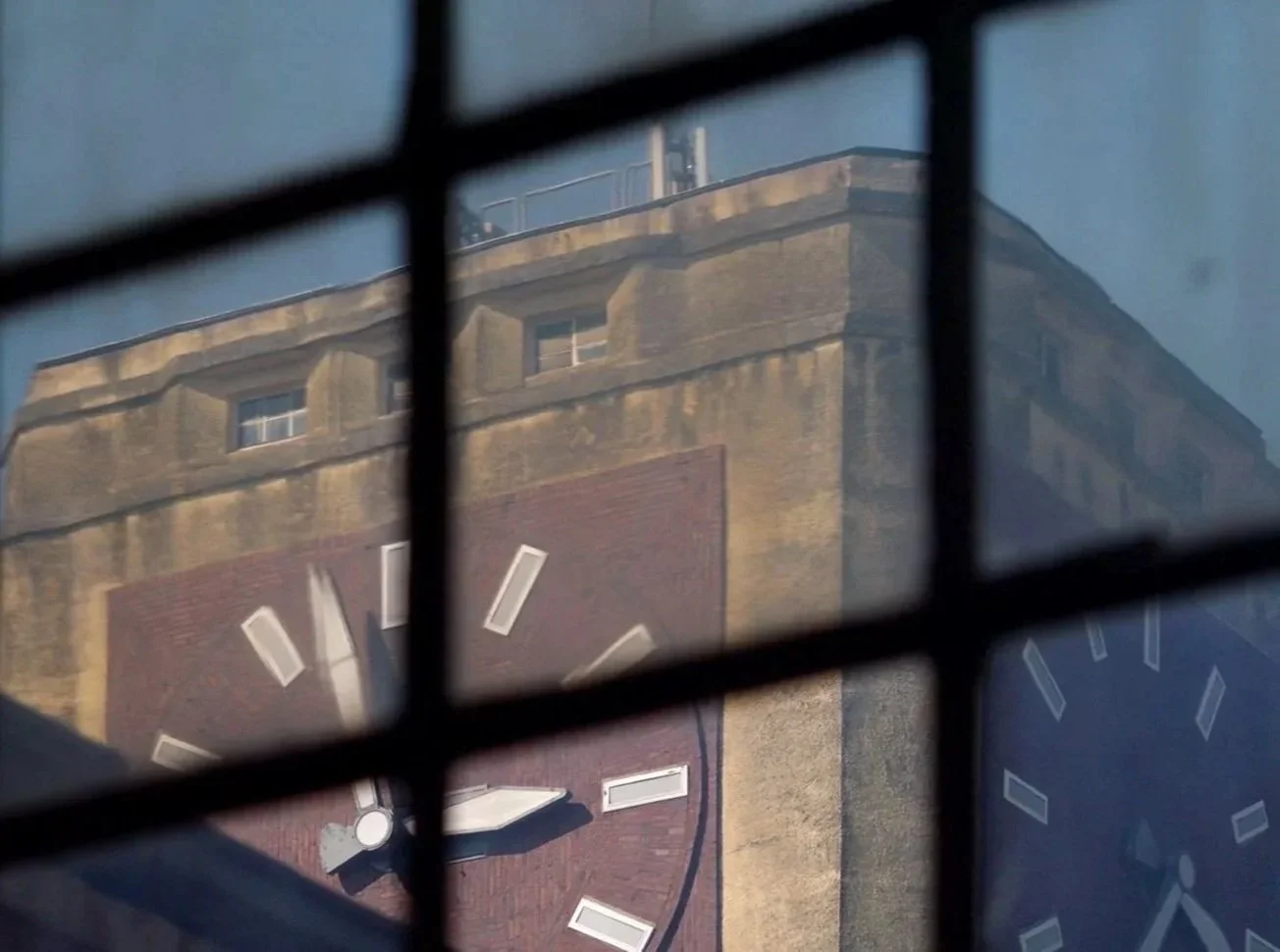 Aufnahme eines alten Gebäudes mit einer großen Uhr, gesehen durch ein Gitter.