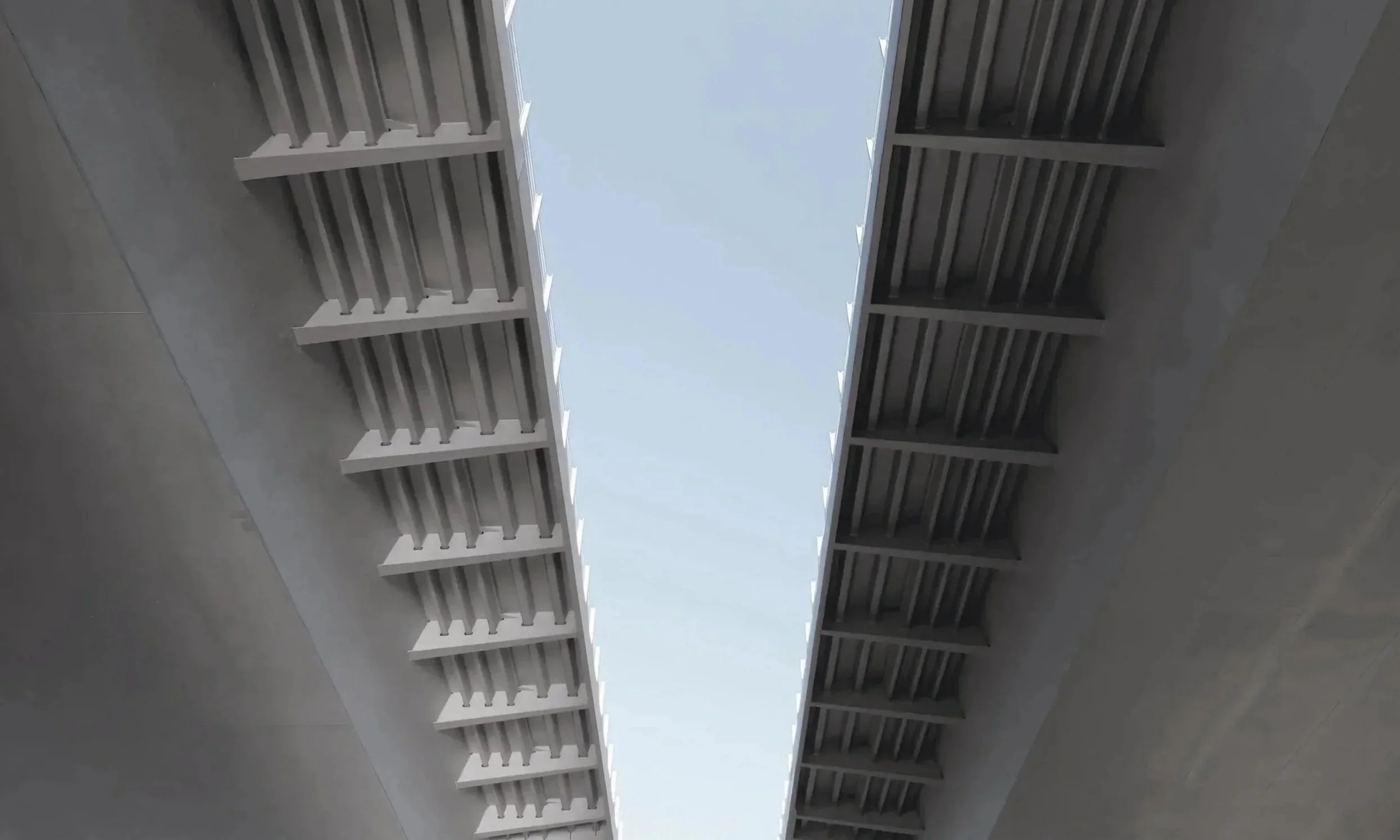 Blick nach oben auf eine Brücke mit Stahlträgern und einem offenen Himmel darüber.