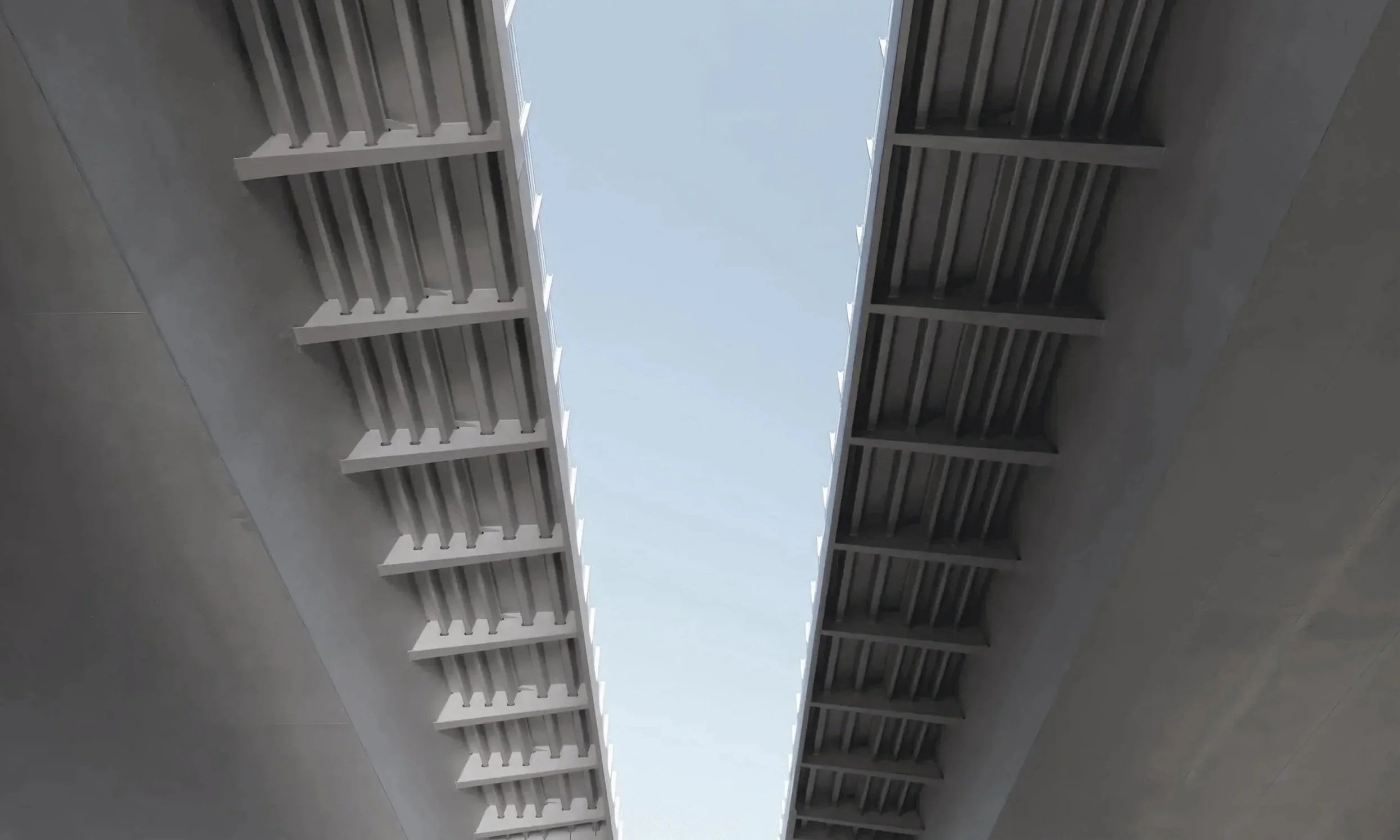 Blick nach oben auf eine Brücke mit Stahlträgern und einem offenen Himmel darüber.