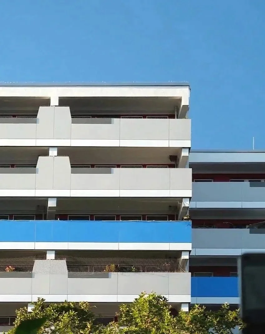 Sicht auf eine moderne Mehrgeschosswohnanlage mit weißen und blauen Balkonen bei sonnigem Himmel