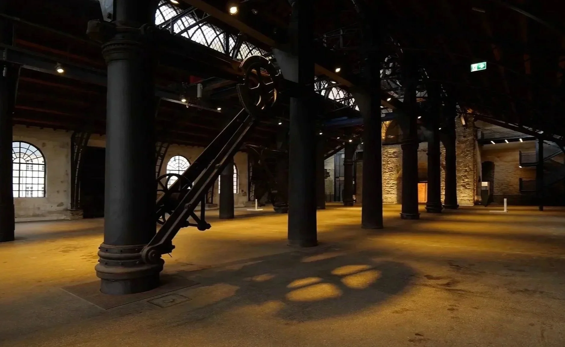 Ein großes, verlassene Fabrikhalle mit Steinsäulen, alten Maschinen und hohen Fenstern, die natürliches Licht hereinlassen.