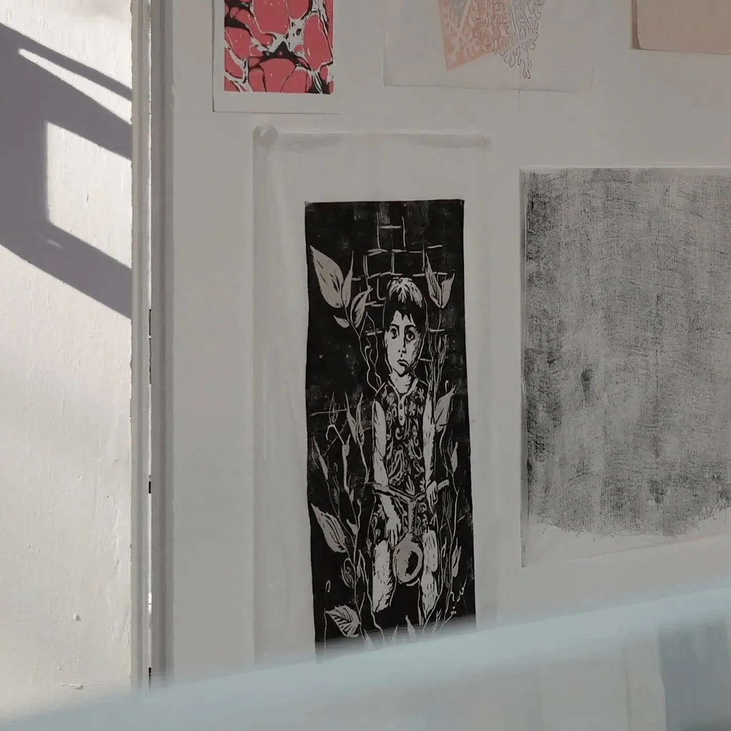 Schwarzes und weißes Kunstwerk eines jungen Mädchens mit kurzen Haaren, umgeben von Blumen, an einer weißen Wand, mit weiteren abstrakten Kunstwerken darüber.