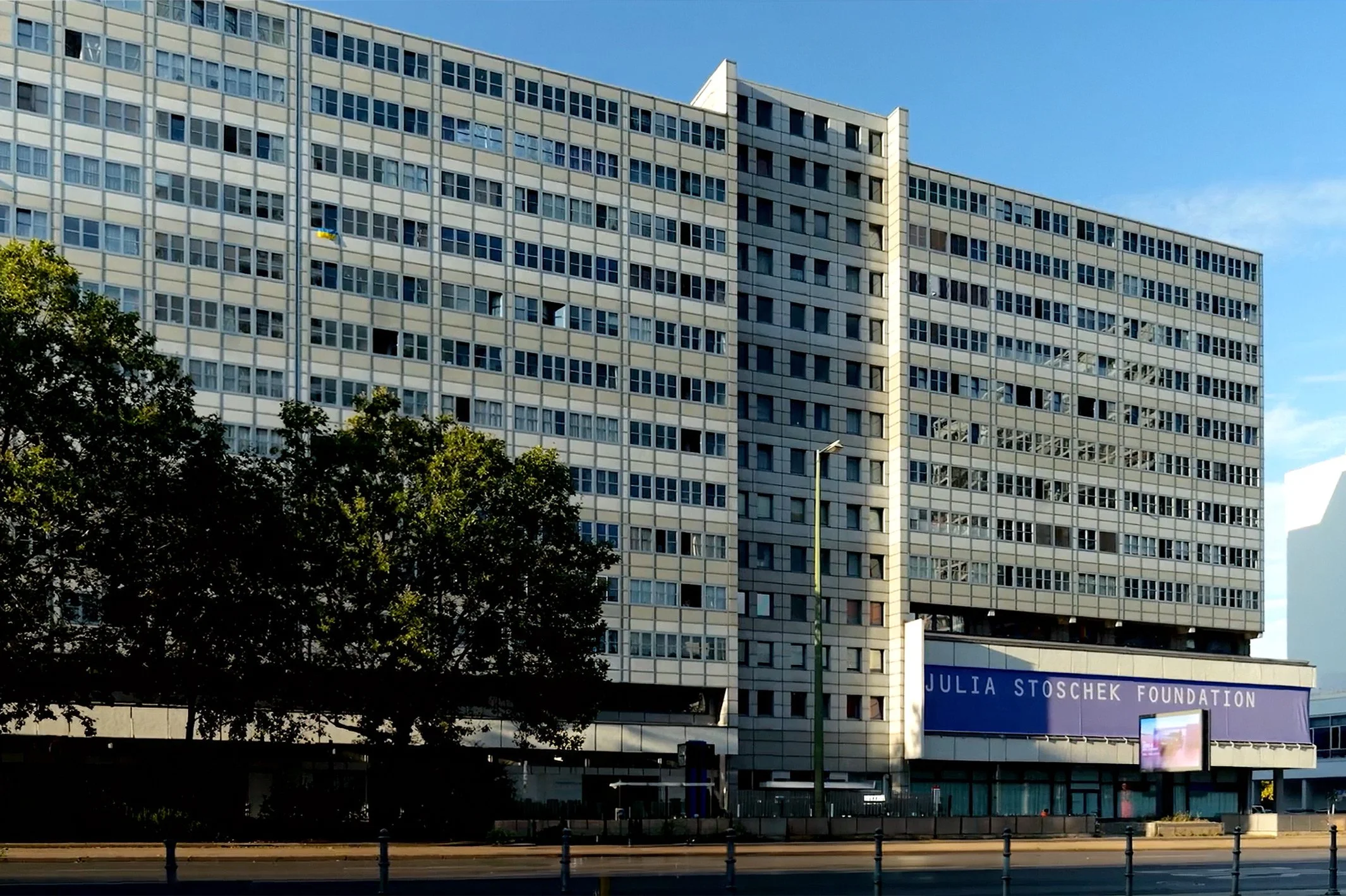 Ein großes mehrstöckiges Gebäude mit unregelmäßig angeordneten Fenstern unter einem blauen Himmel, mit Bäumen im Vordergrund und einem Schild, das die Julia Stoschek Foundation anzeigt.