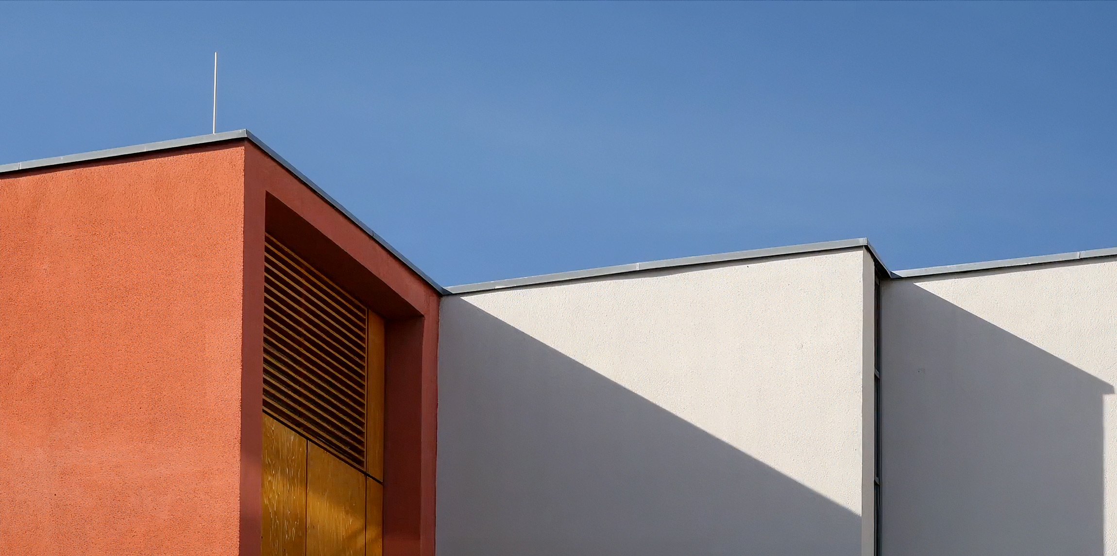 Nahaufnahme der eckigen Farbigen Fassade eines modernen Gebäudes mit rotem und weißem Putz und blauer Himmel im Hintergrund.