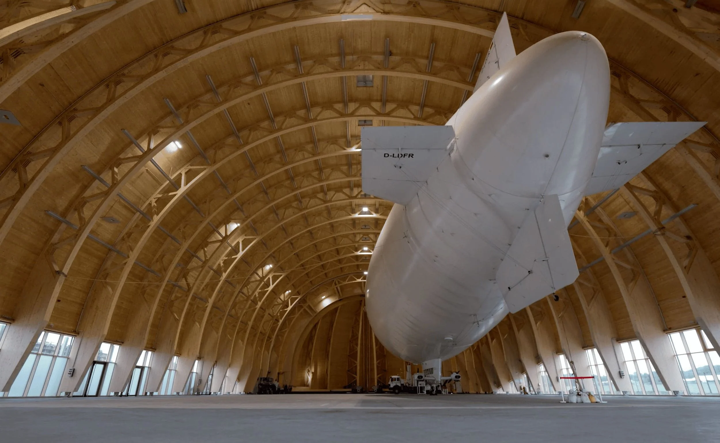 Ein großes weißes Luftschiff befindet sich in einer Holzhalle mit hohen, gewölbten Decken.