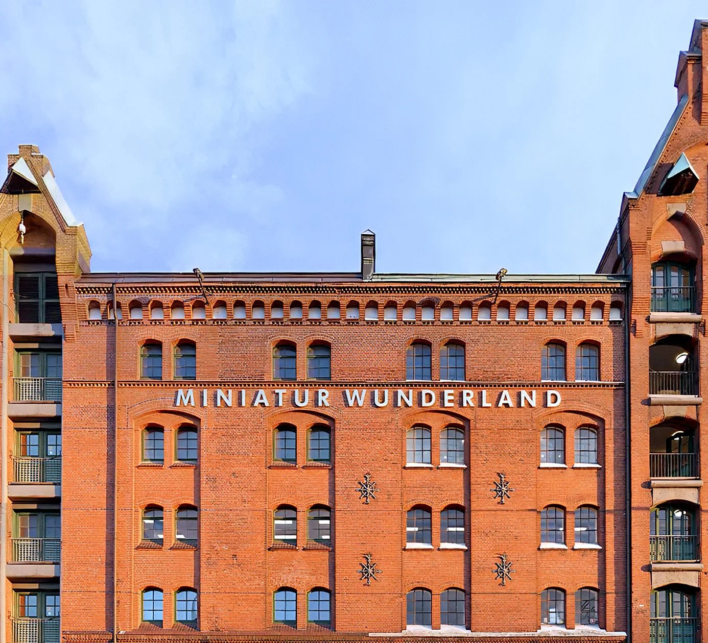Ein rotes Backsteingebäude mit weißen Buchstaben, die 'Miniatur Wunderland' sagen, und mehreren Fenstern, mit einem blauen Himmel im Hintergrund.