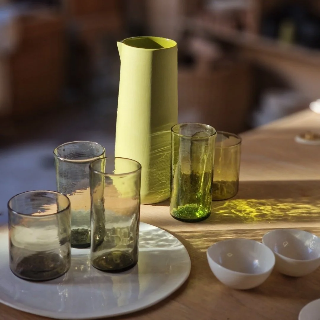 Un groupe de verres et petits bols sur une table en bois, avec un vase vert en arrière-plan.