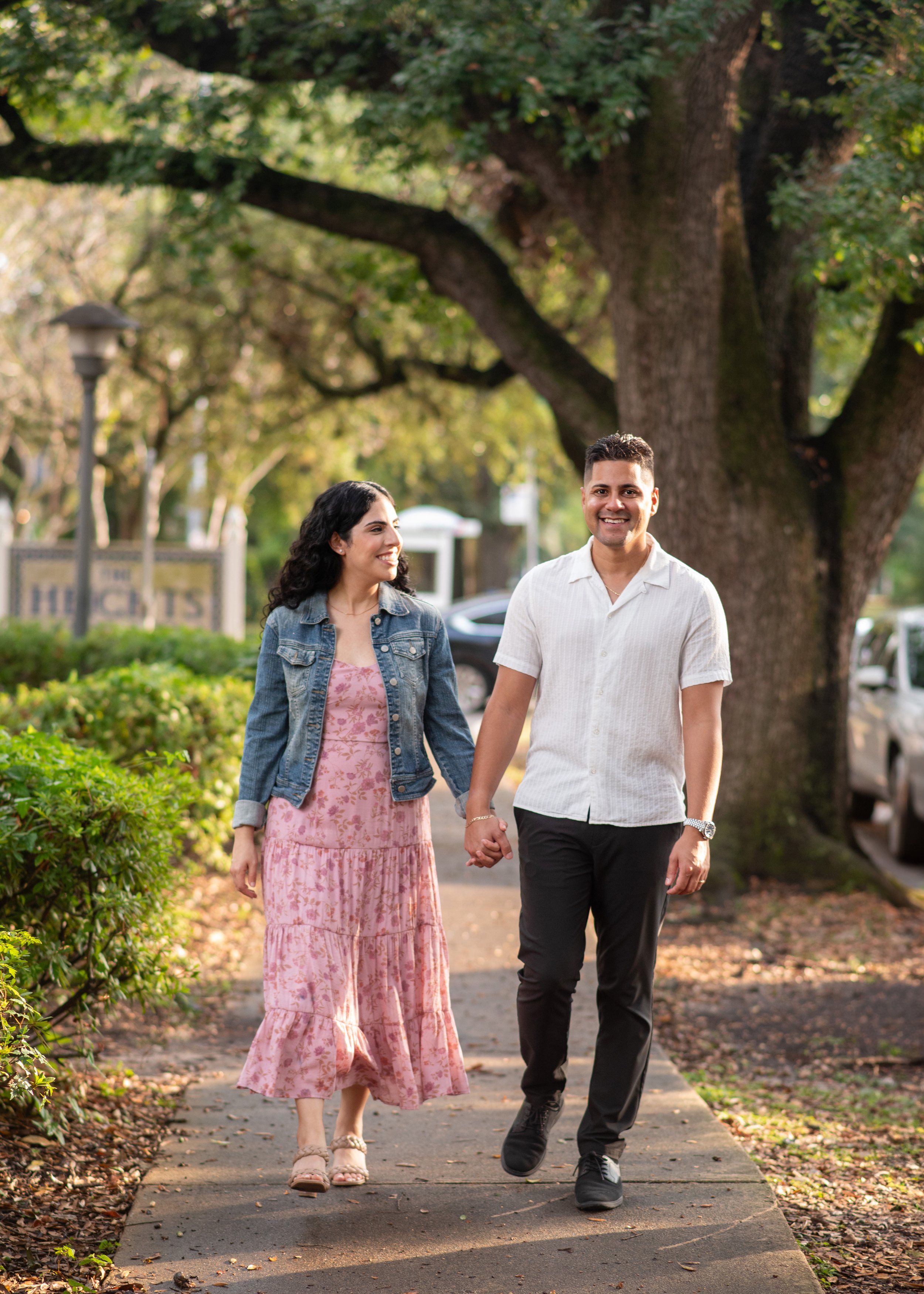A couple walking hand-in-hand in a tree lined neighborhood for headshots in Houston.