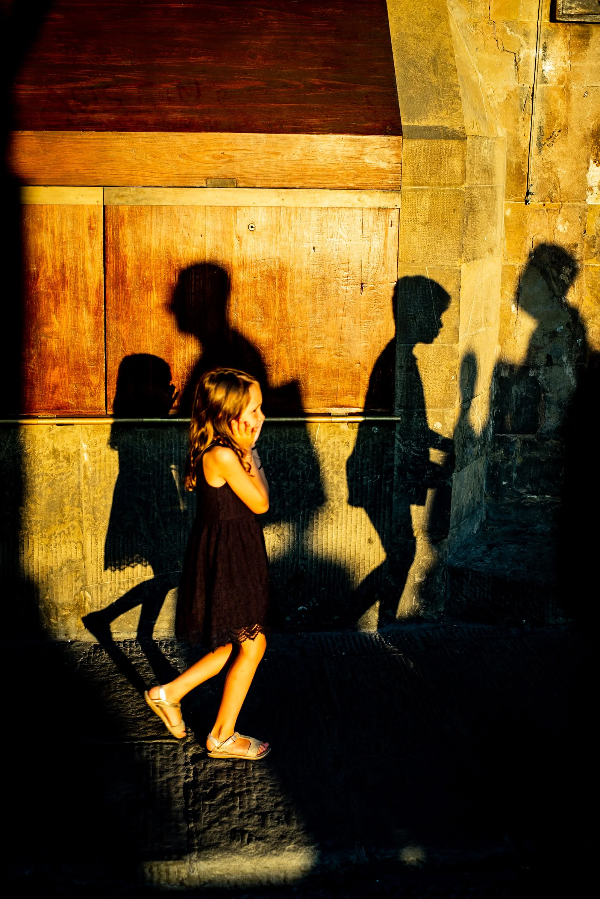 Young girl lit by golden sun and framed by shadows of passersby