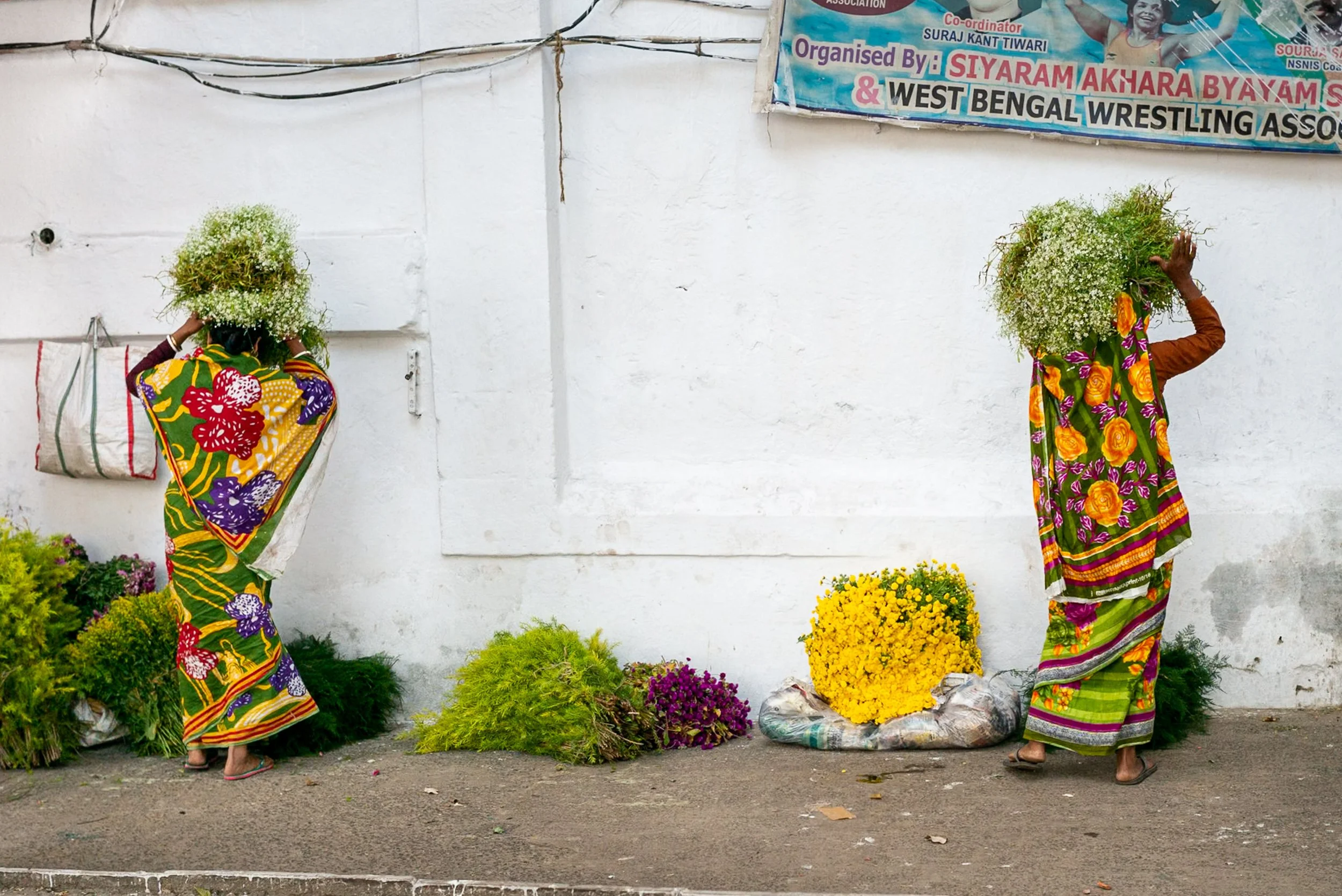 Two Indian women in saari carrying bunches of flowers in mirroring position