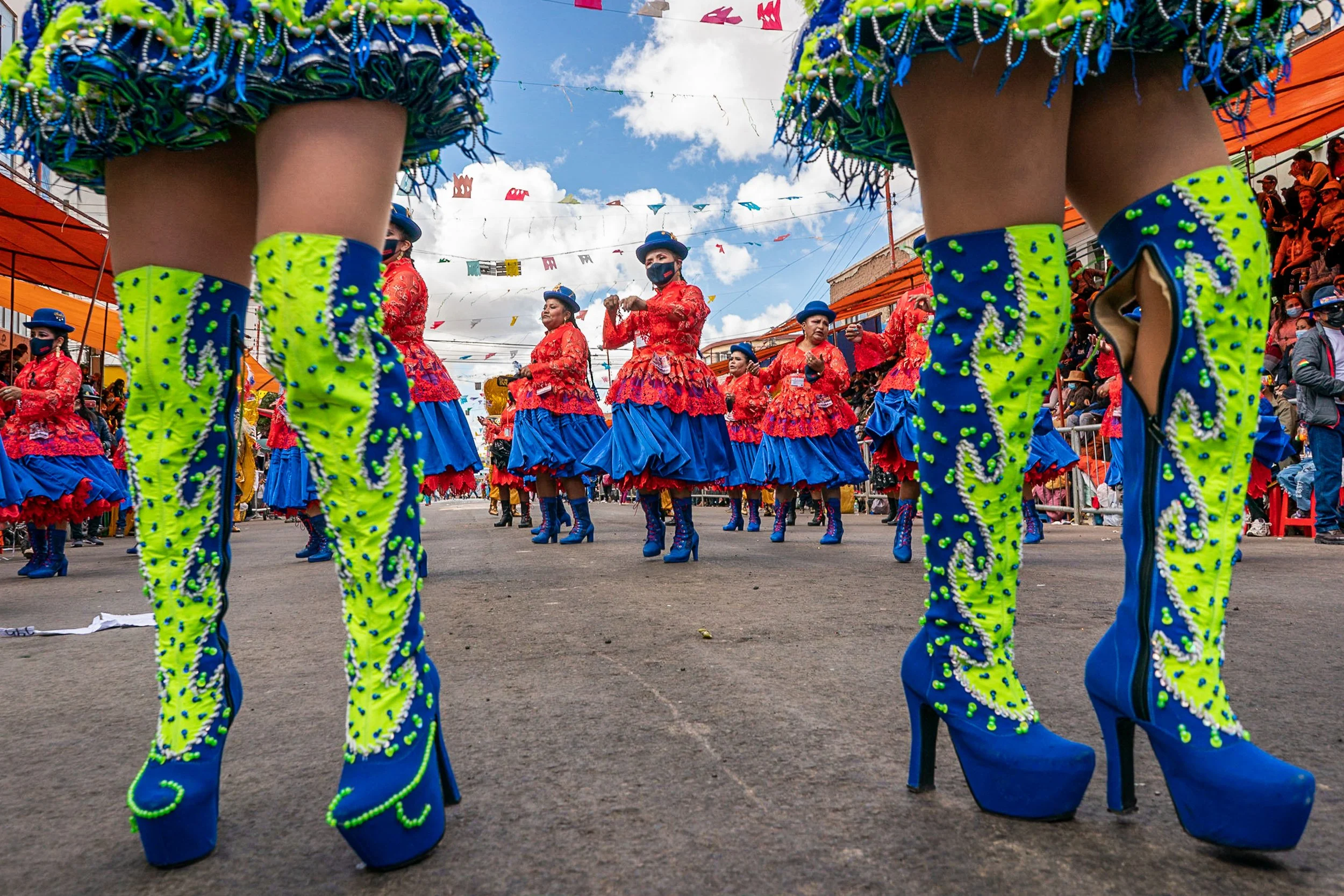 Morenada dancers framed by legs of other dancers in Oruro, Bolivia