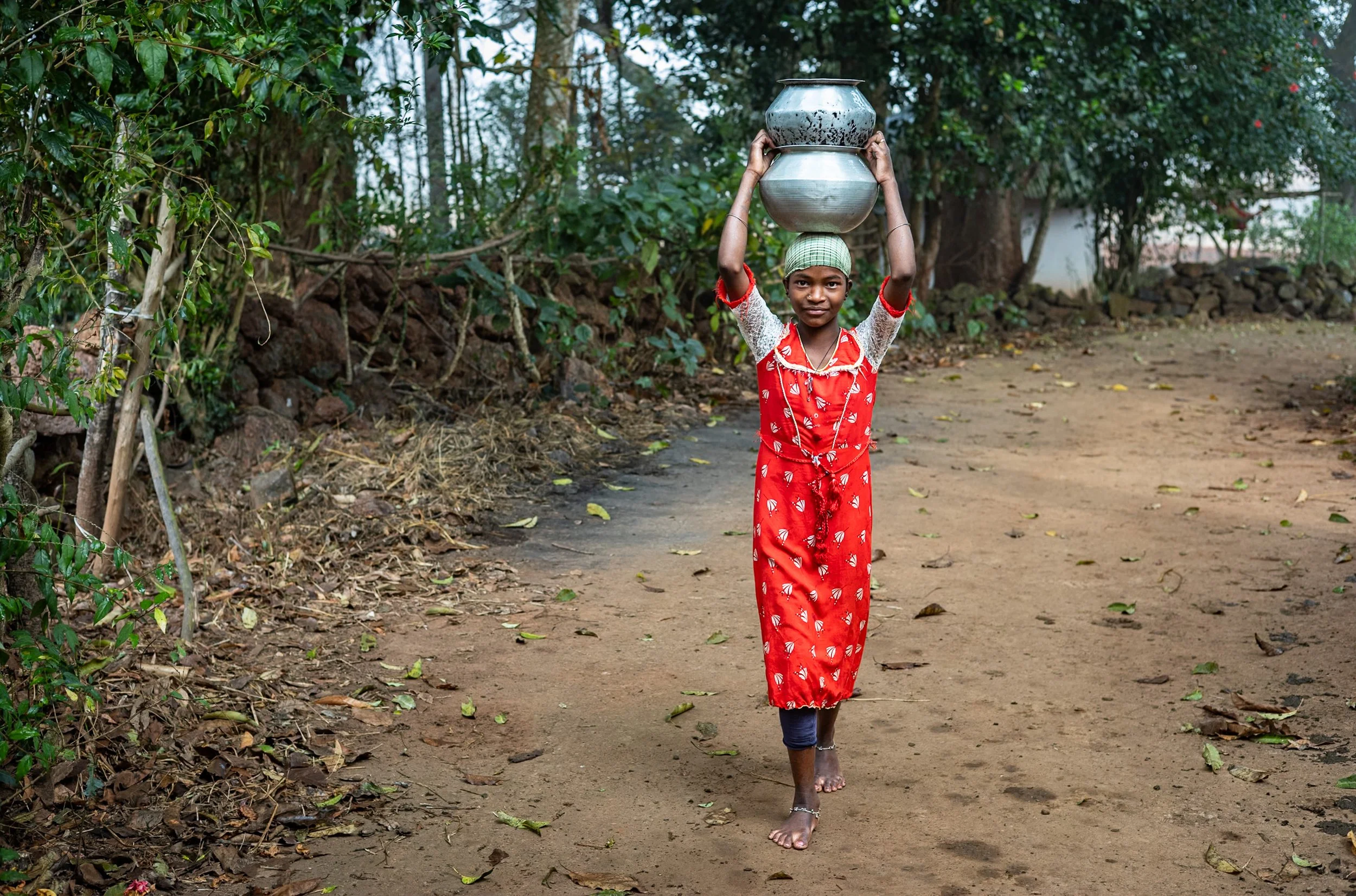 Portrait of girl in red dress carrying jars on head