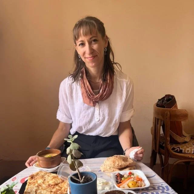 Woman seated at a dining table with bread, soup, salad, and a potted succulent