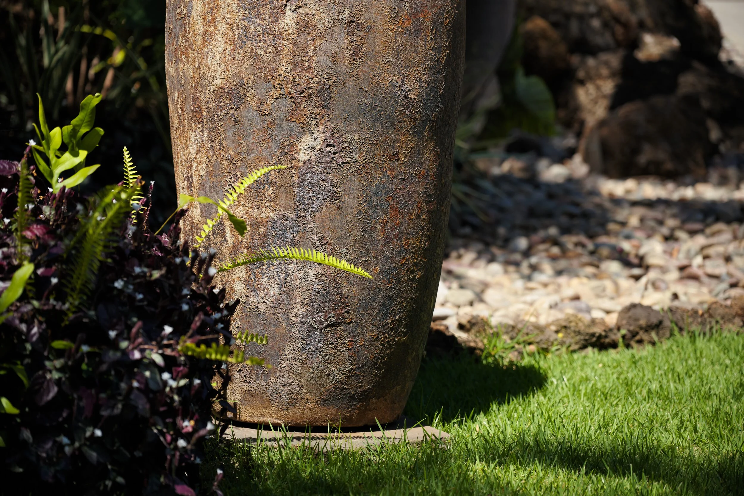 Close-up of a rusted metal garden sculpture with plants and grass in the background.