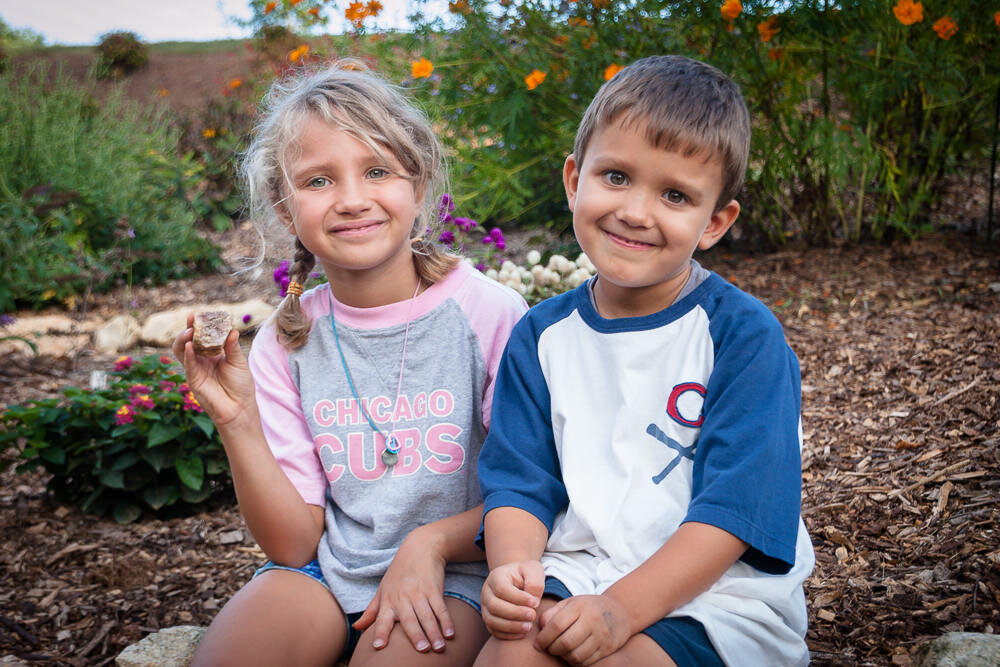 sister and brother sit in a garden and smile for the camera