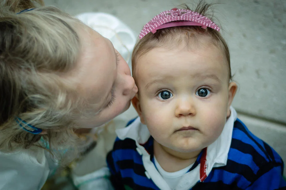 little girl kisses her baby brother wearing a tiara on the cheek