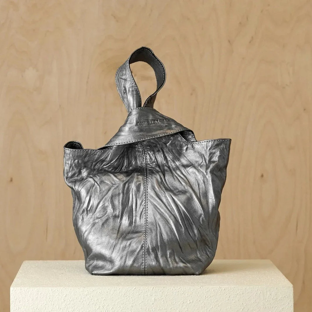 A single loop rises from a folded peak to make the handle: carry it as an elegant clutch, a striking handbag or a functional crossbody bag depending on your destination. We have it in two leathers, crinkled pewter and a black-and-white stripe, and we