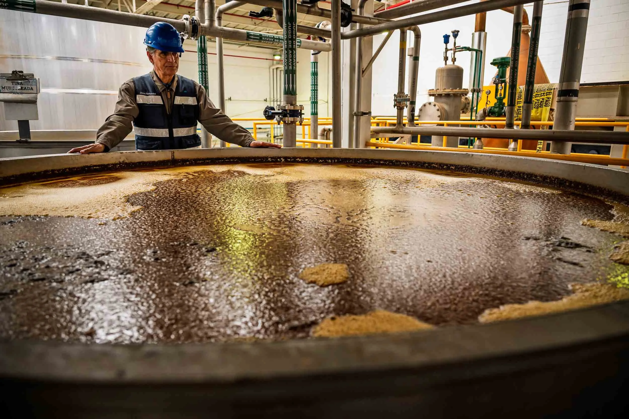 Maestro tequilero monitoreando la fermentación en una tina de madera gigante dentro de una destilería, fotografía para editorial cultural.