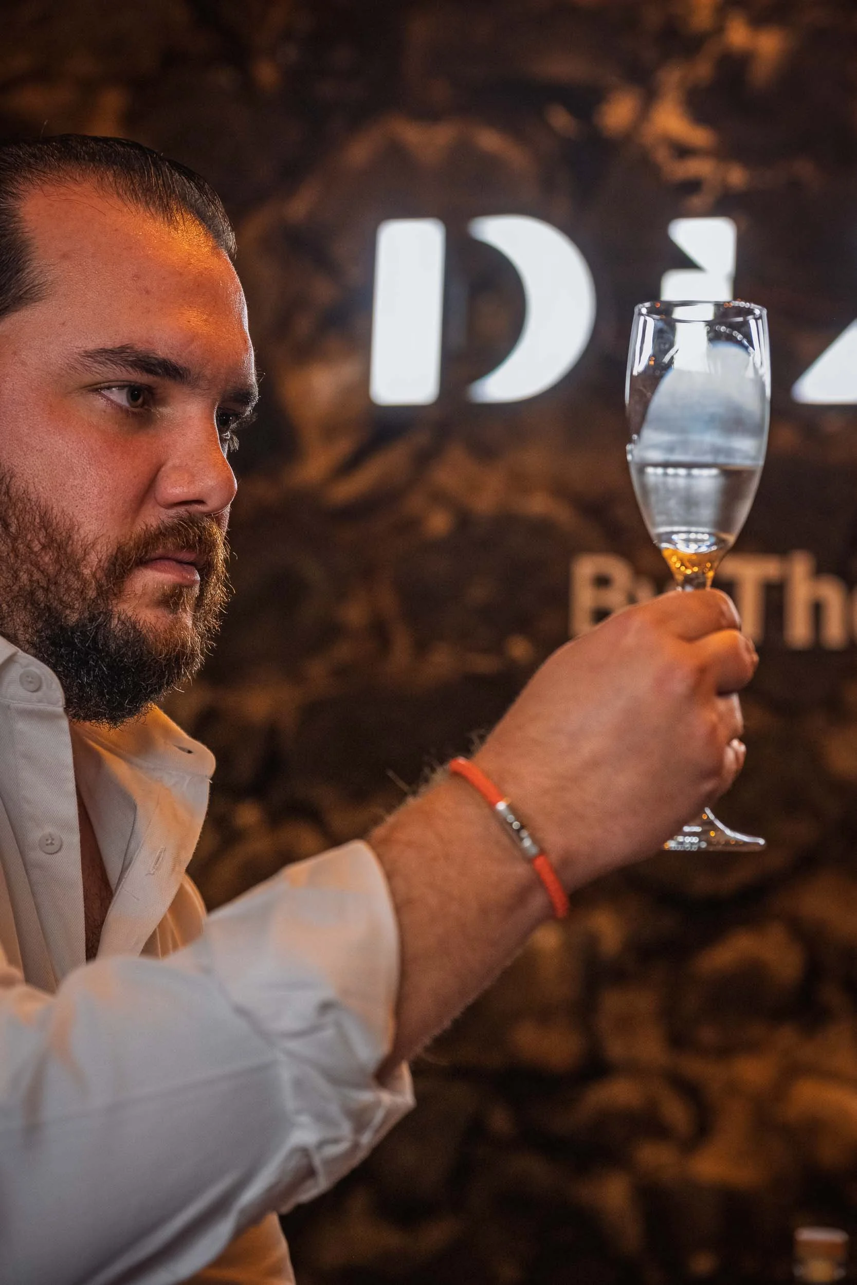 Bruno Barba sosteniendo una copa de cristal con mezcal en una cata profesional dentro de una mezcalería, retrato editorial cultural.