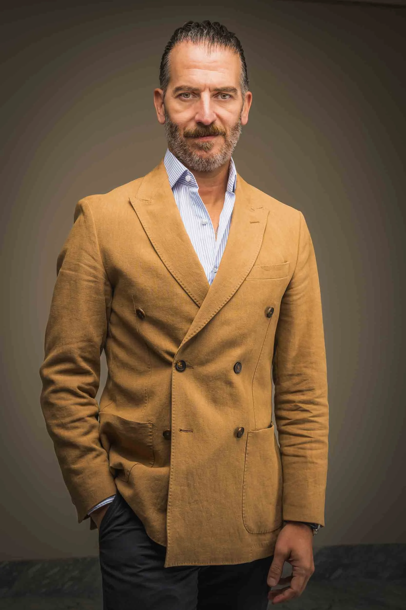 Retrato ejecutivo de un hombre con saco camel y camisa a rayas, en estudio con fondo cálido. Fotografía por Rodrigo Ojeda.
