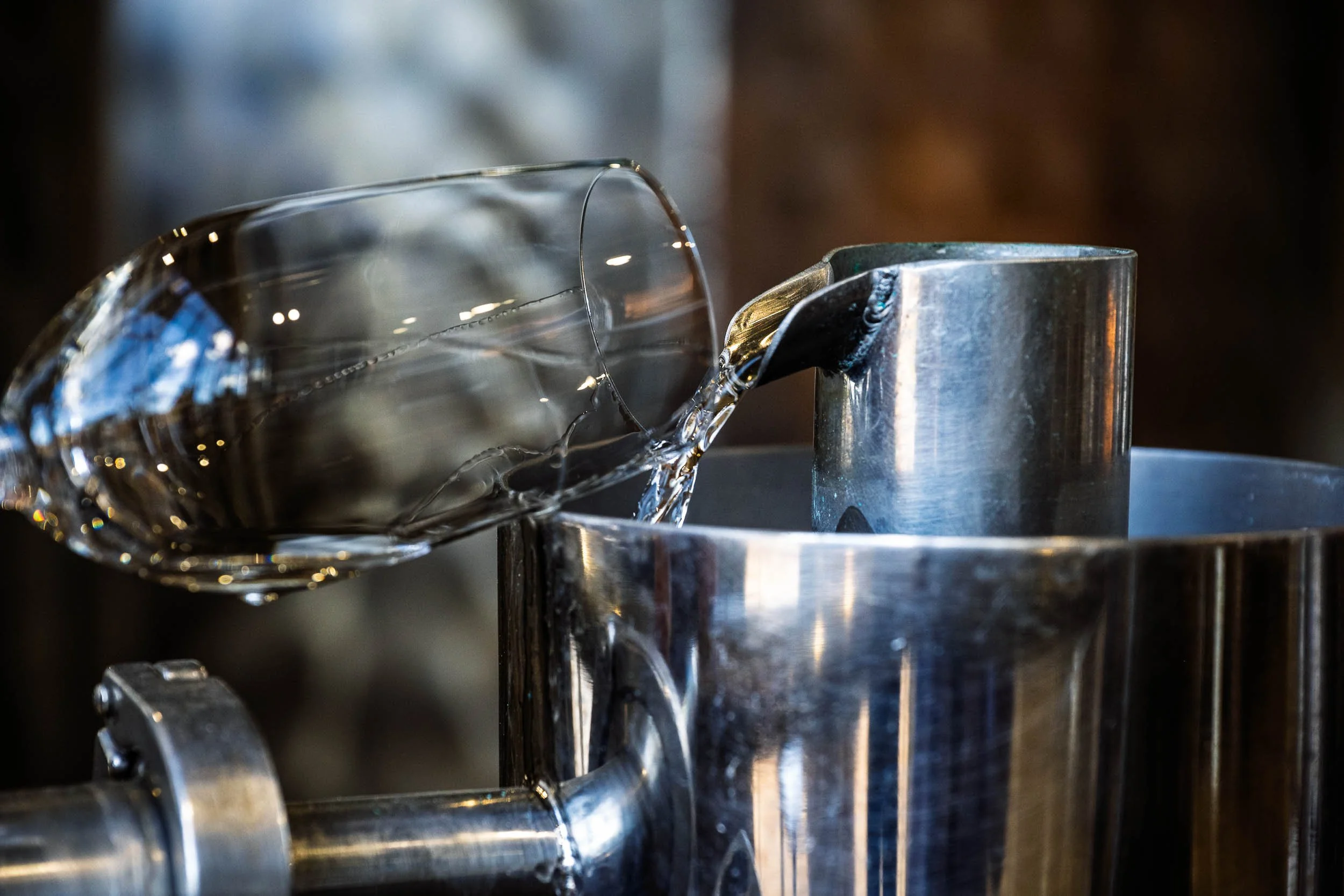 Imagen vertical de un destilador verteriendo tequila en un recipiente metálico, resaltando la precisión del proceso y la pureza del líquido.