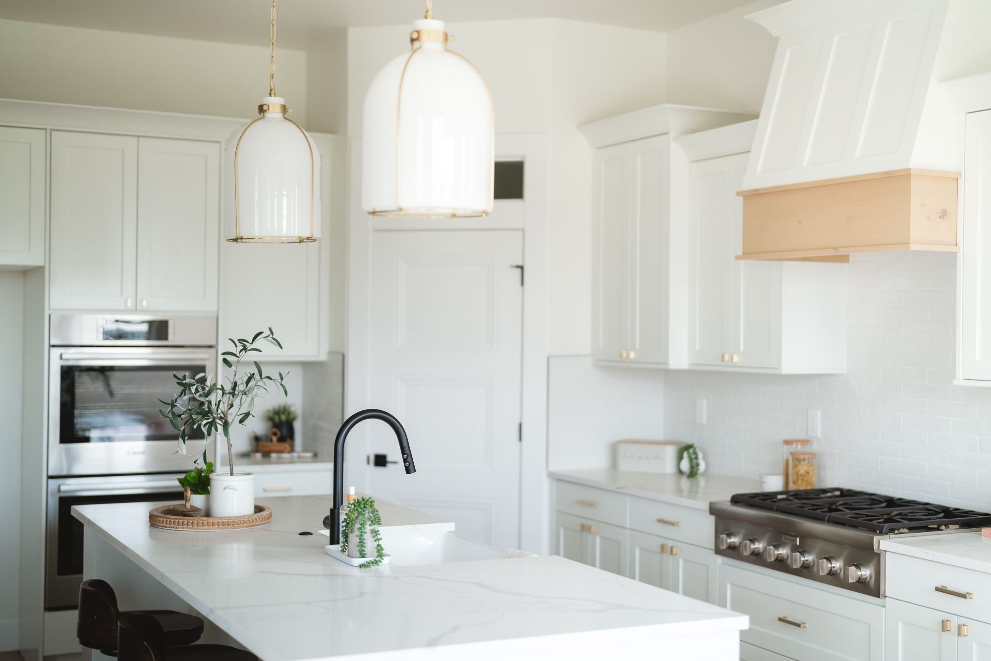 Modern kitchen interior with white cabinets, a marble island countertop with a black faucet, pendant lights, stainless steel oven, and a gas stove.
