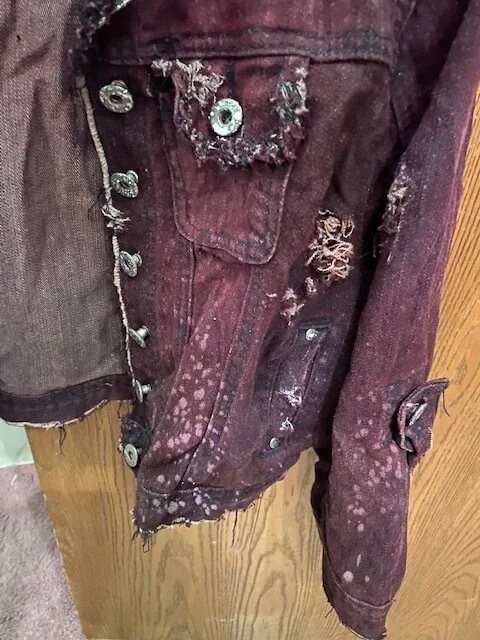 The jacket was distressed using a razor blade then dyed using Rit wine color dye. Once heat set, white spatter was added using a spray bottle and watered down acrylic paint.