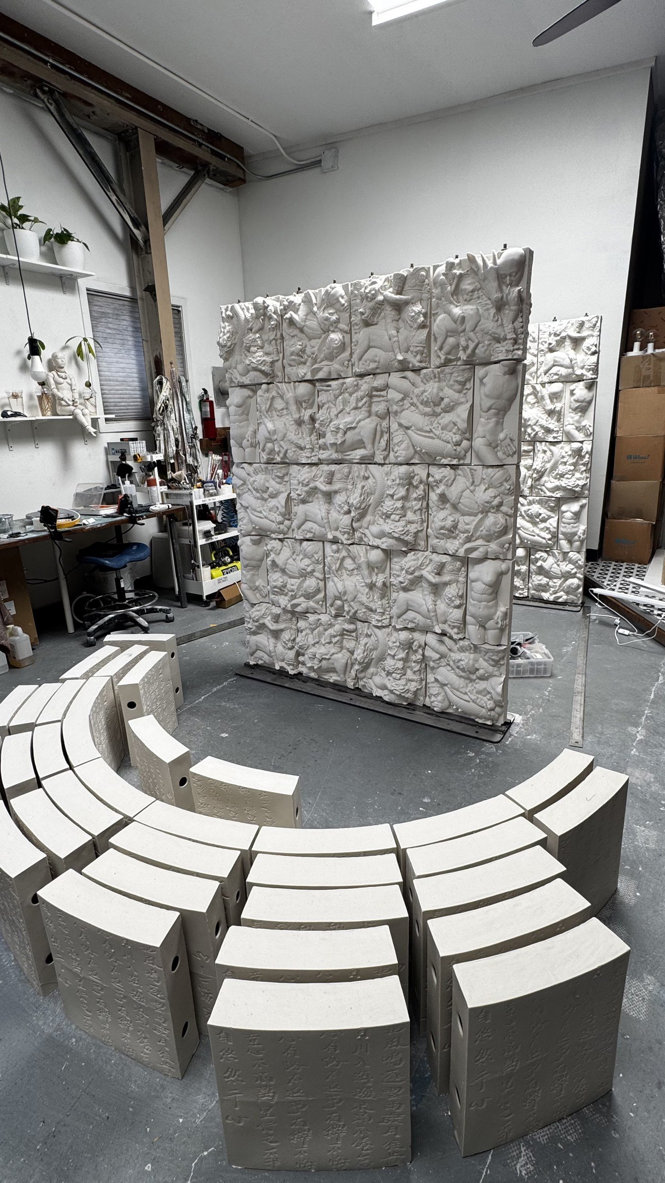 Studio view of assembled relief panels with curved ceramic units laid out on the floor.