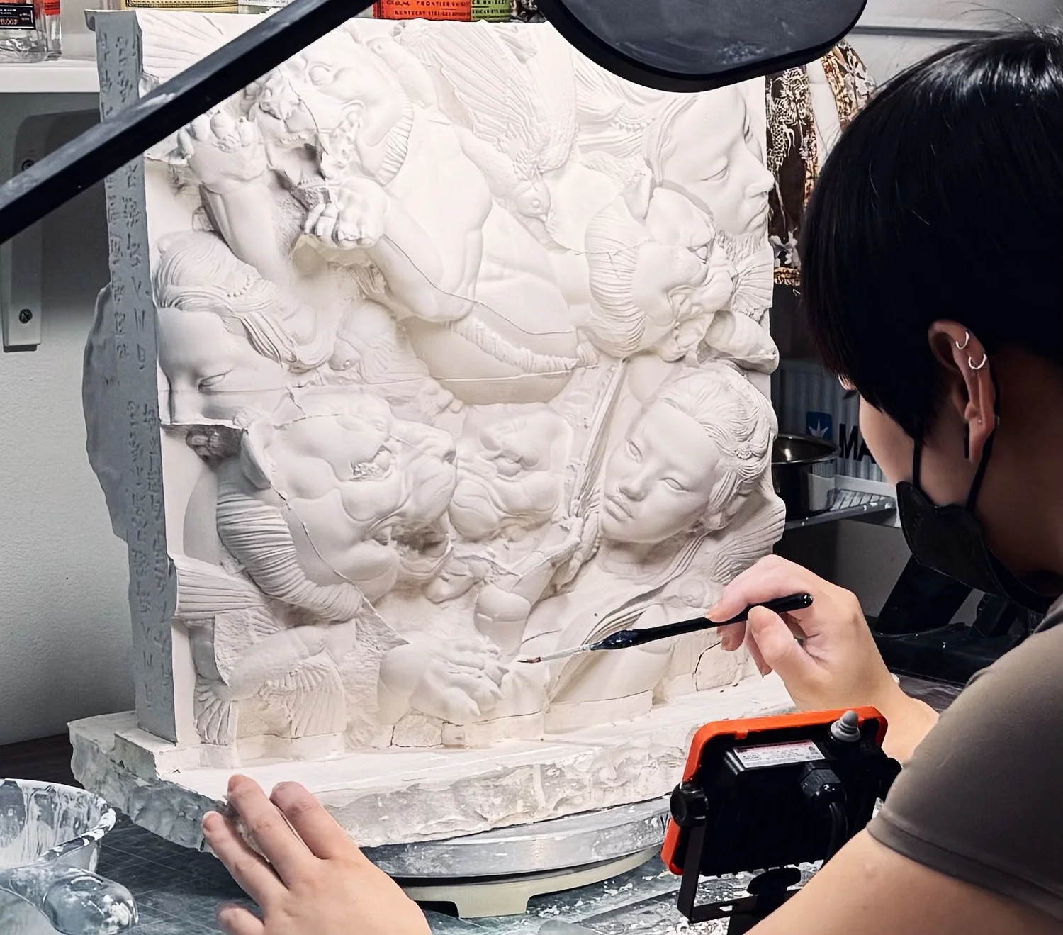 Studio view of a person using a small brush to work on a relief panel.