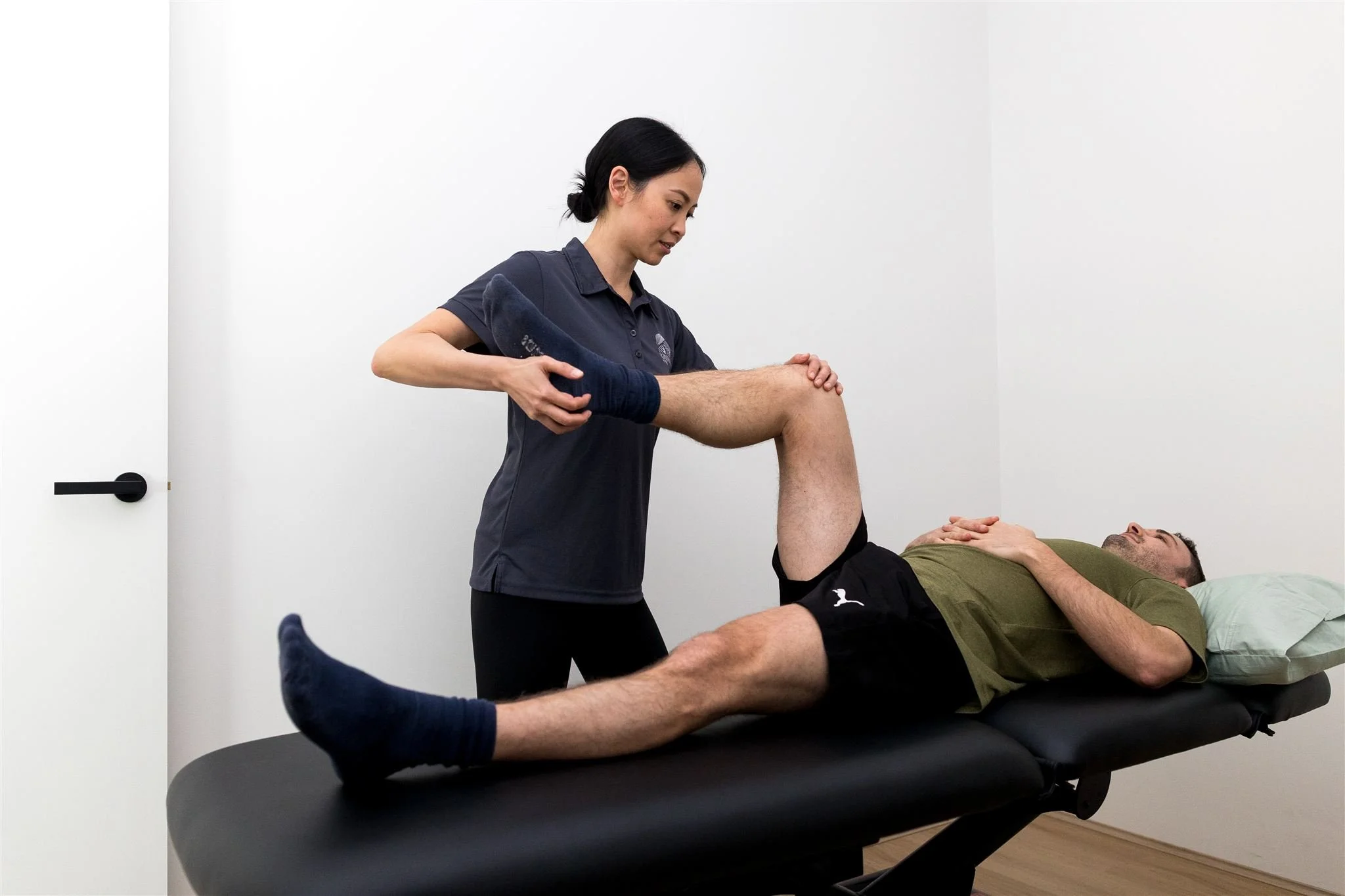 Female physiotherapist assessing knee mobility and movement of a male client during a clinical exercise assessment at Kinima Physio