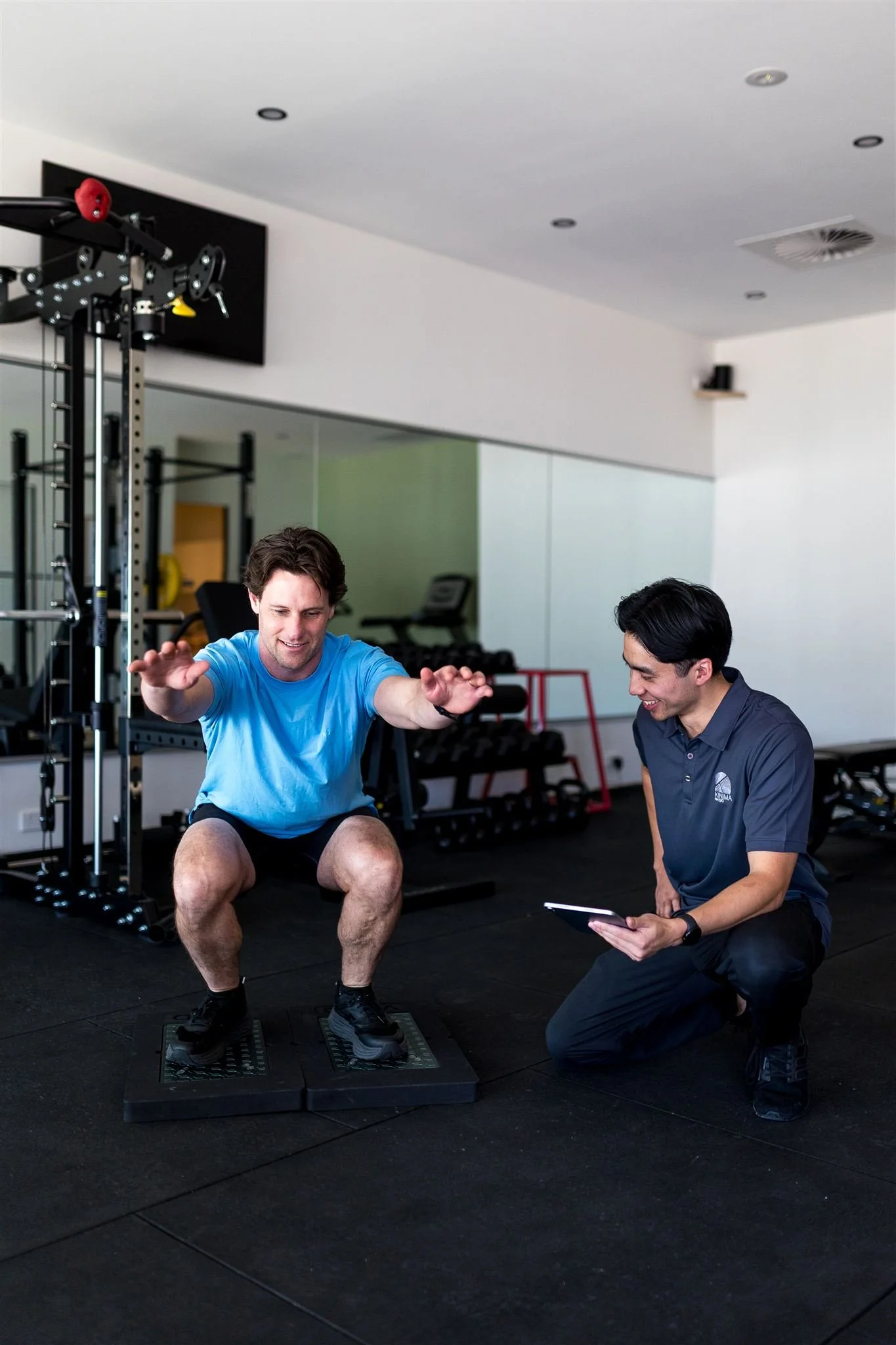 Male physiotherapist assessing a male client performing a squat using objective force plate data during a clinical exercise assessment