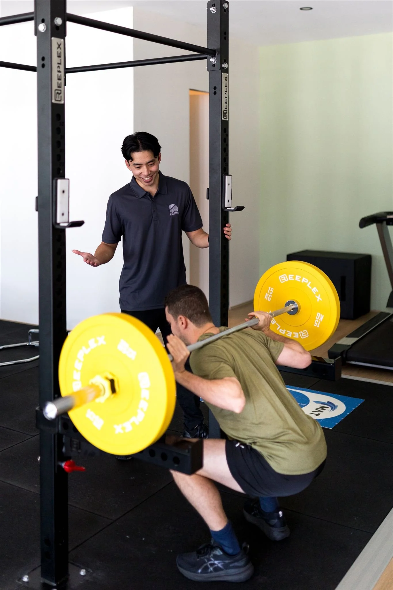 Man being instructed by a Physiotherapist performing a back squat in the rehabilitation gym at Kinima Physio
