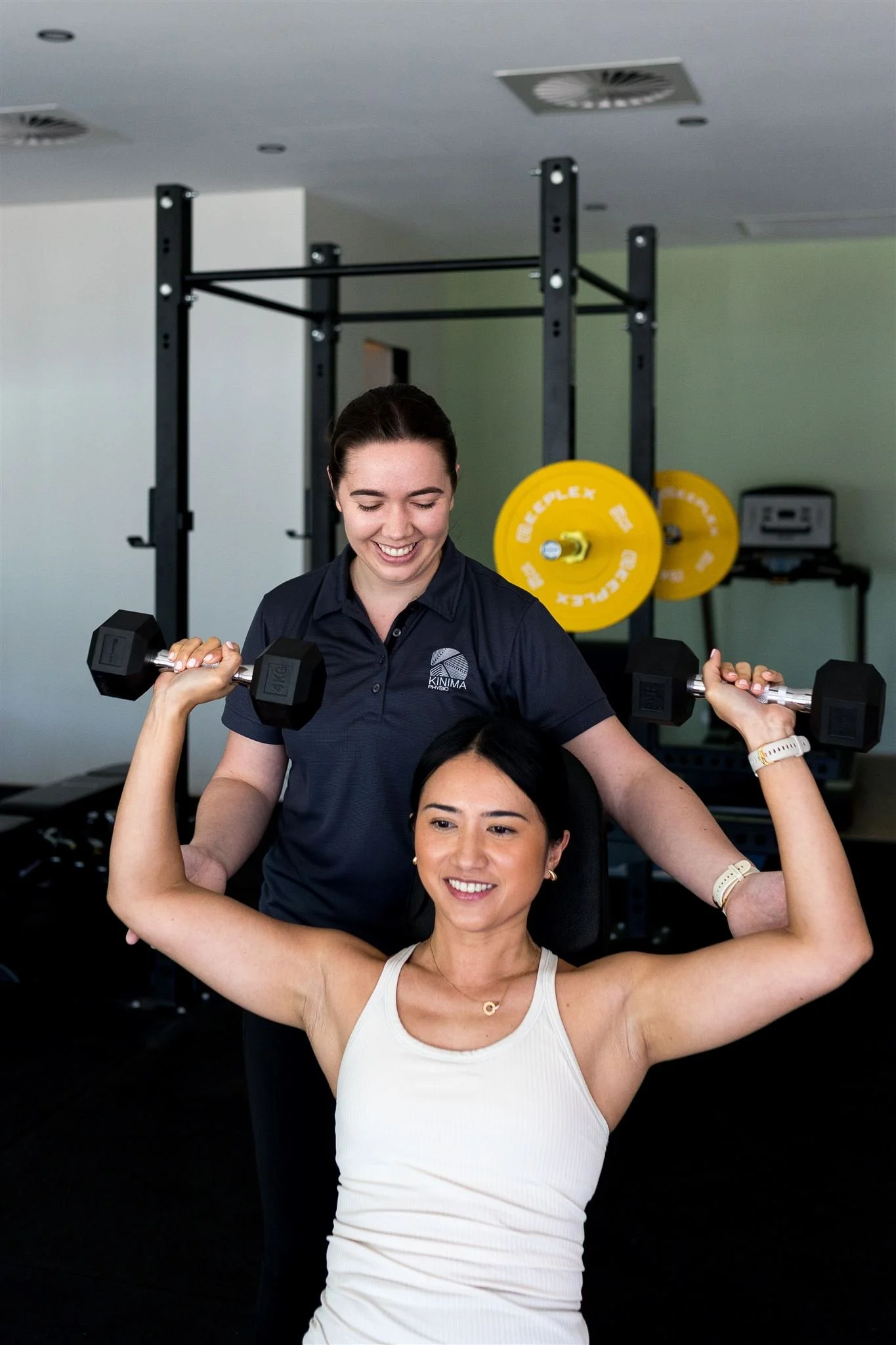Female physiotherapist supervising a client through a dumbbell shoulder press exercise