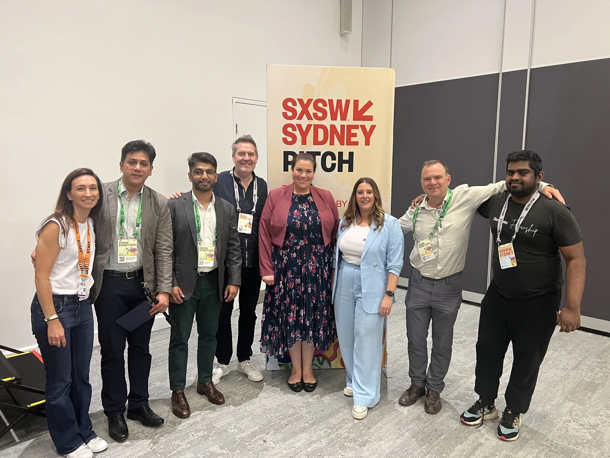 A group of nine people standing together at SXSW Sydney event, smiling for the camera, with a SXSW Sydney sign in the background.