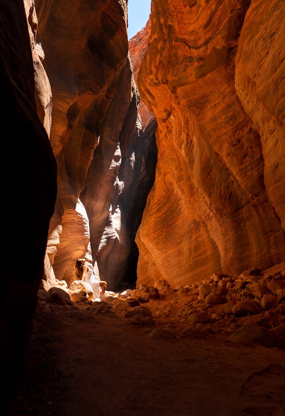 A woman seated in an orange sandstone slot canyon.