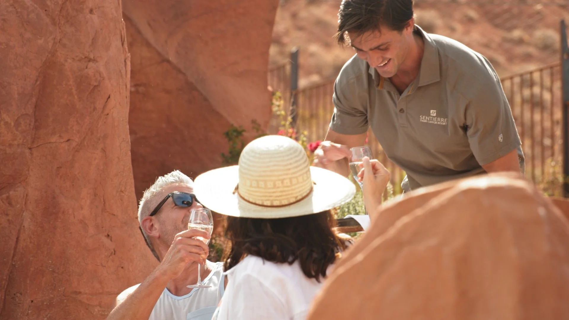 Hospitality team member serving guests at an outdoor table framed by warm sandstone walls.