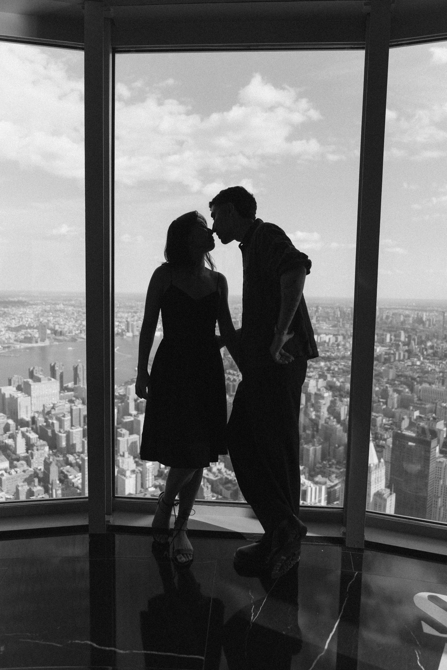 Black-and-white silhouette of Sophia and Mike kissing in front of a city-view window