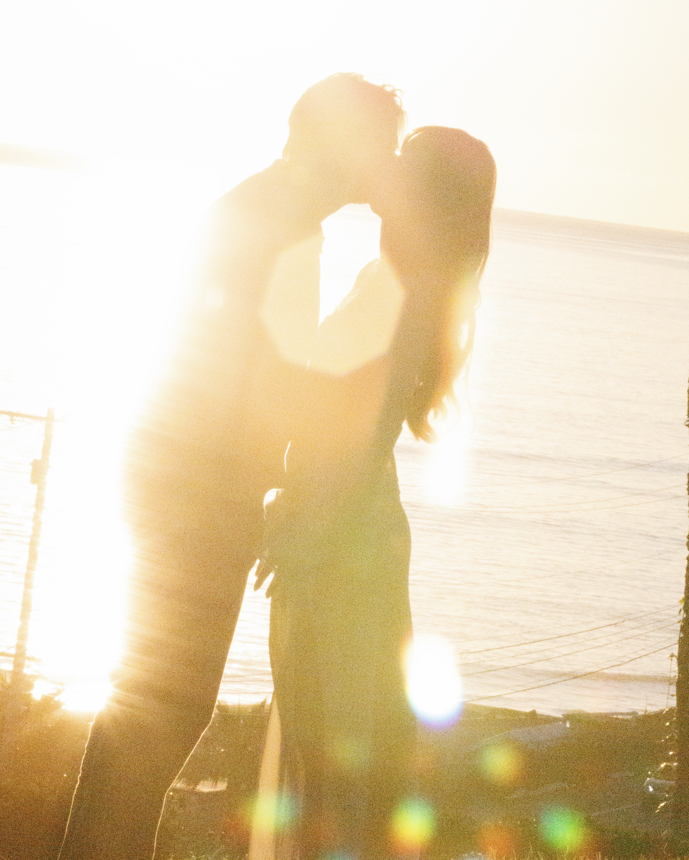Silhouette of a couple kissing during sunset at the beach with bright sunlight and lens flare.