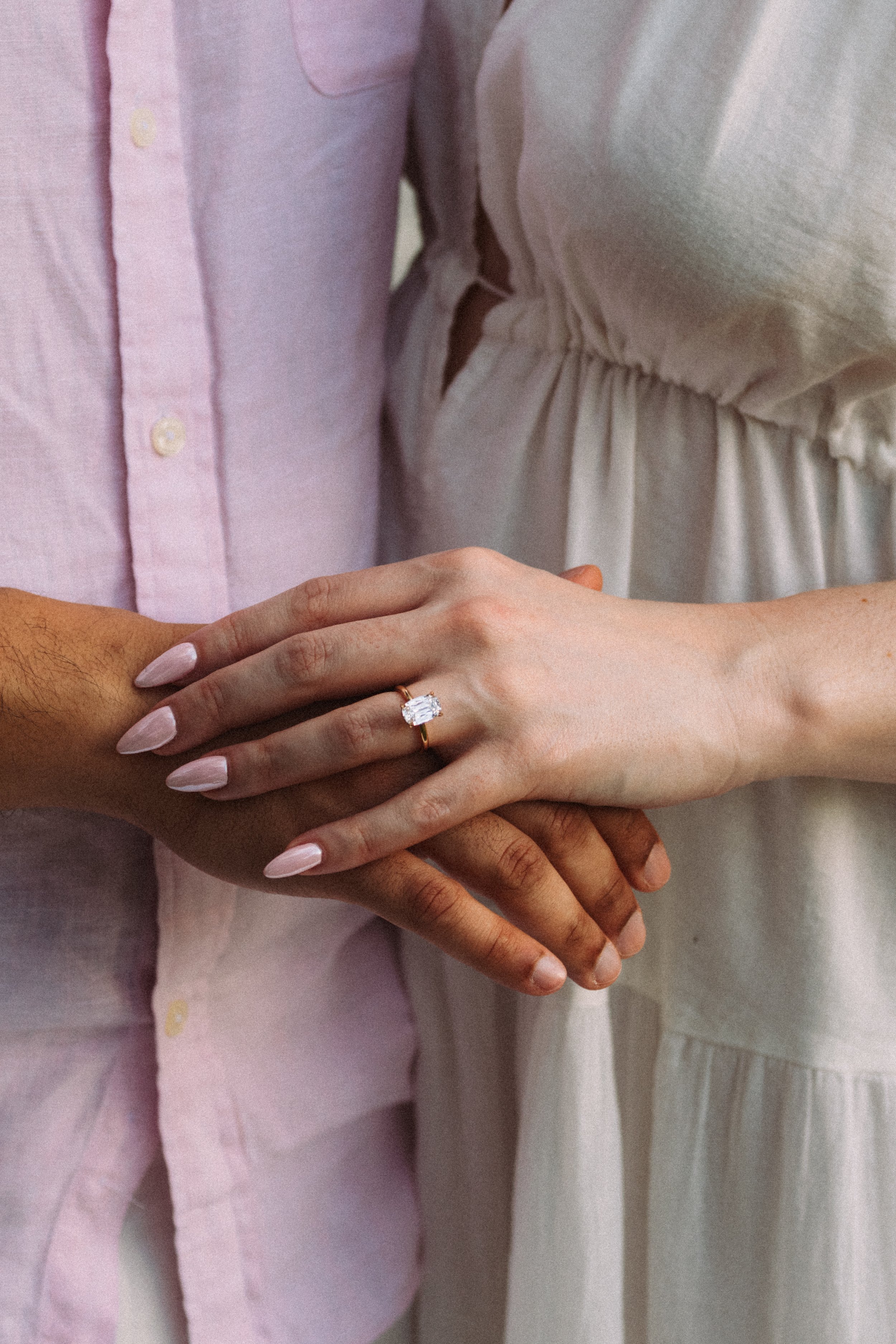 Close-up of two people holding hands, one person wearing a ring with a large rectangular gemstone.