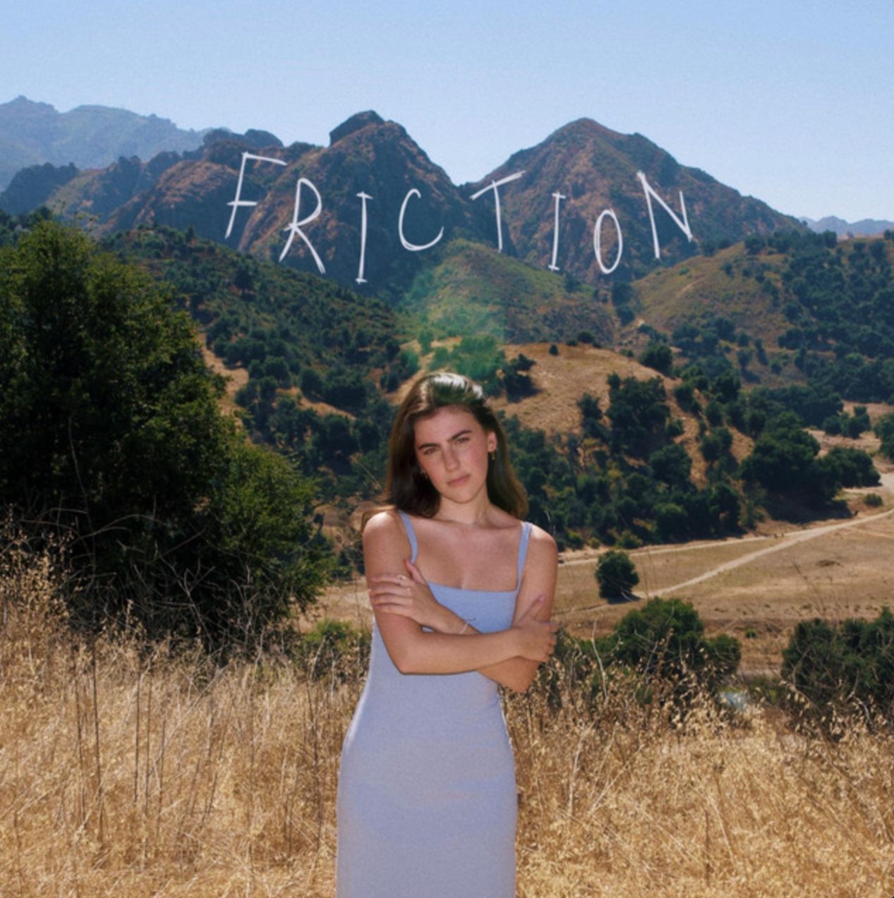 Avery Lynch in a light blue dress standing outdoors in a dry field with hills and trees in the background, with the word "Friction" written across the mountain.