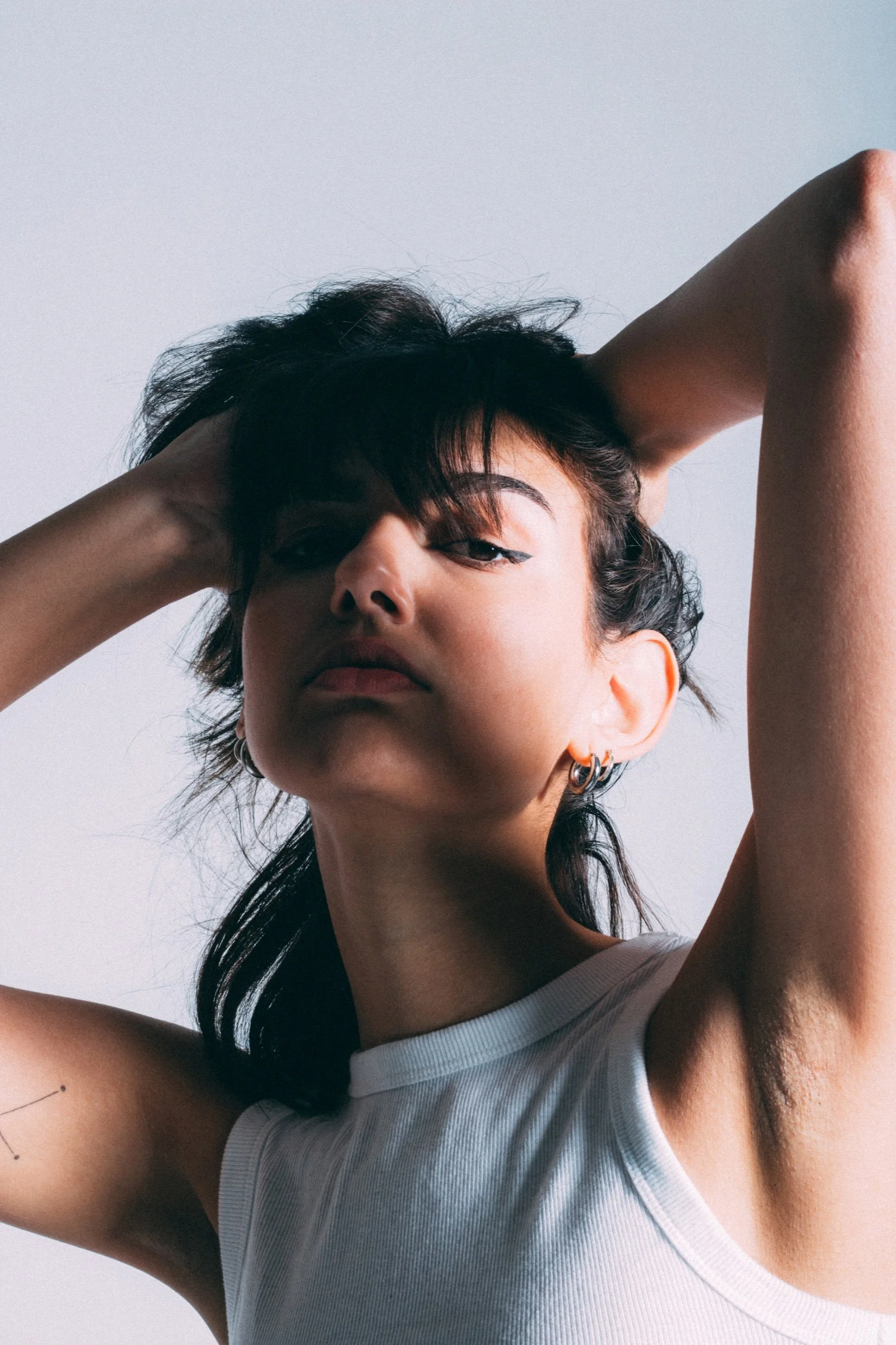 Close portrait in directional light with raised arms and a white ribbed top