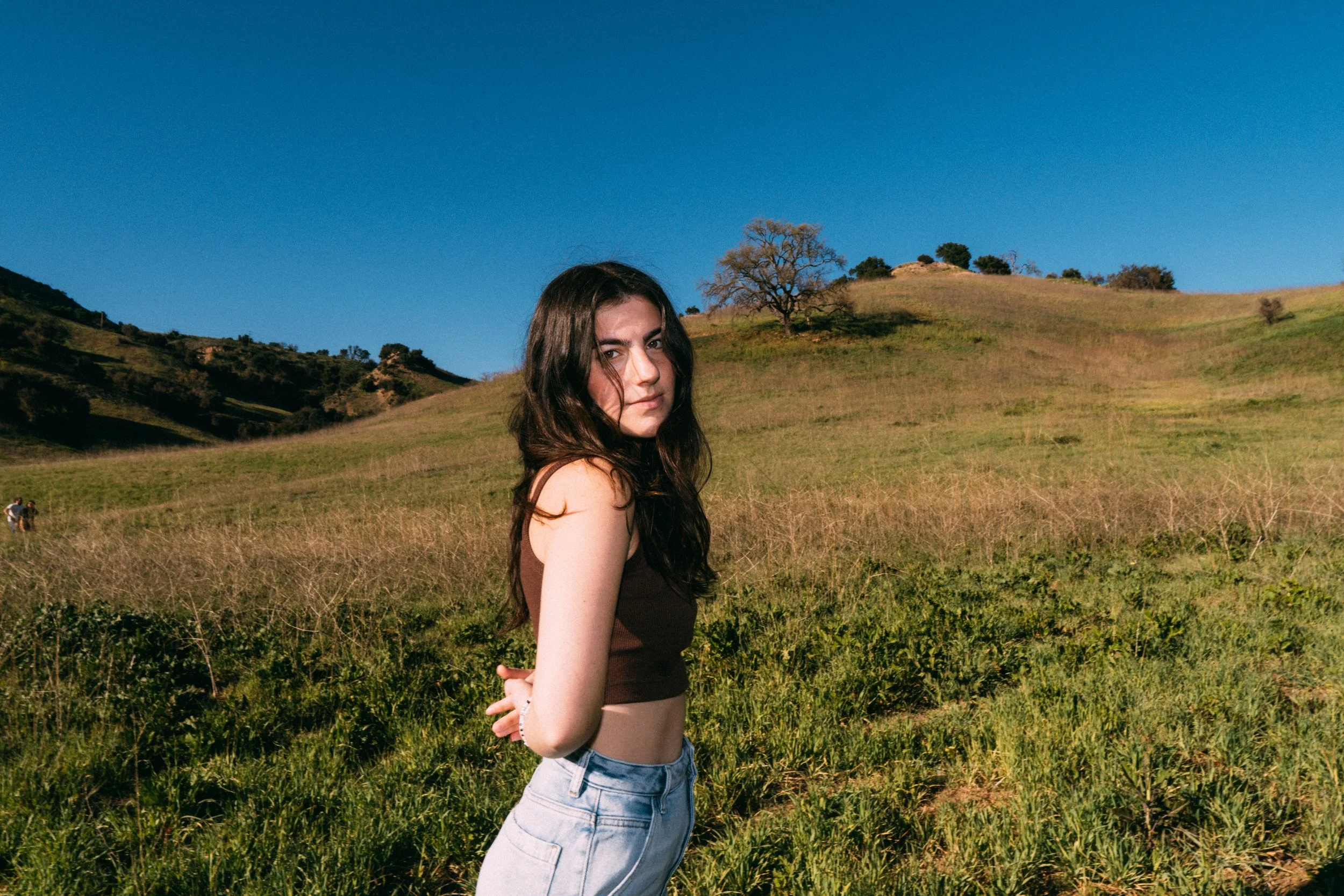 Avery Lynch looking toward the camera in a grassy field beneath a blue sky.