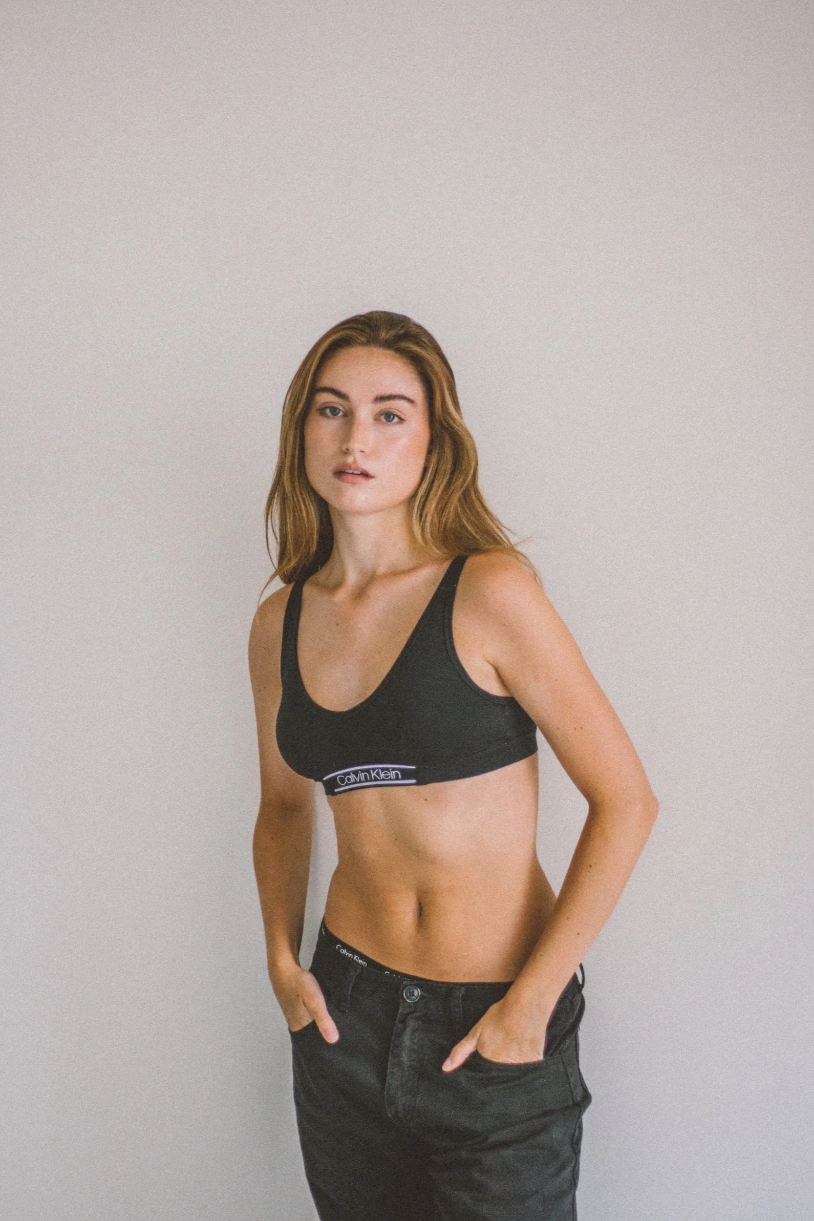 Model in a black athletic top and dark jeans against a plain studio background