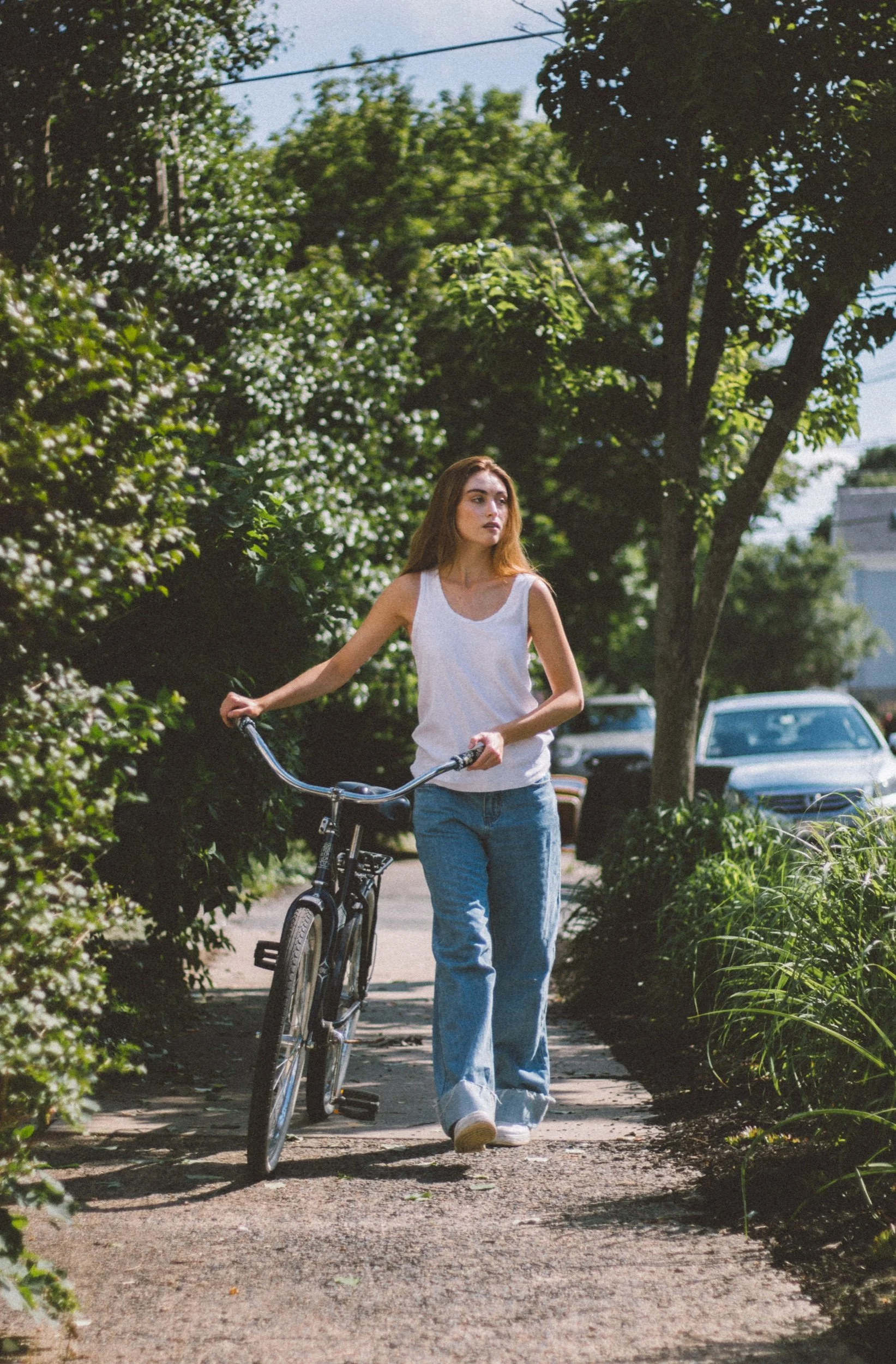 Model in a white tank and loose jeans walking a bicycle outdoors
